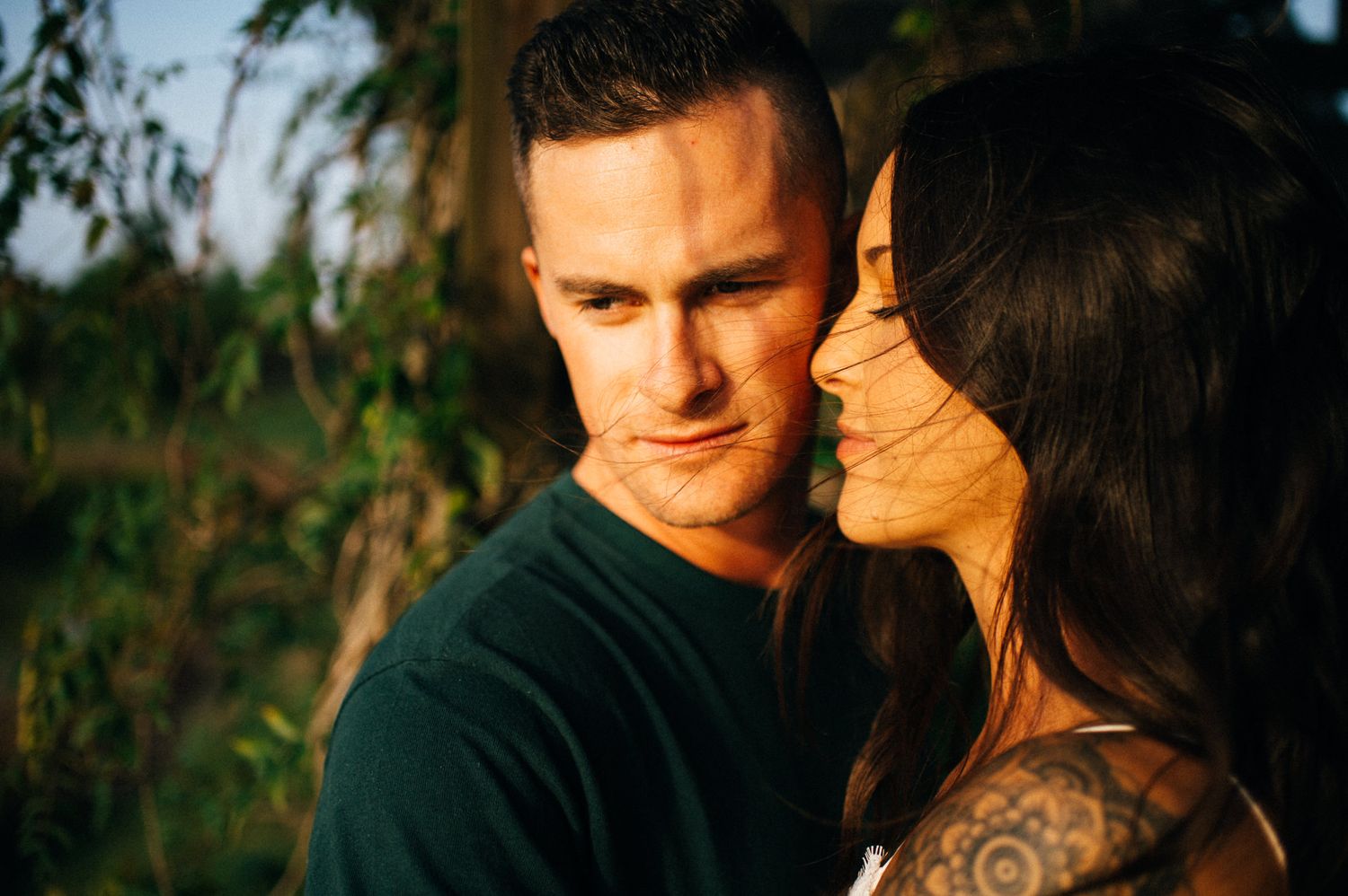 A tender moment between a couple in golden hour lighting amid natural foliage.