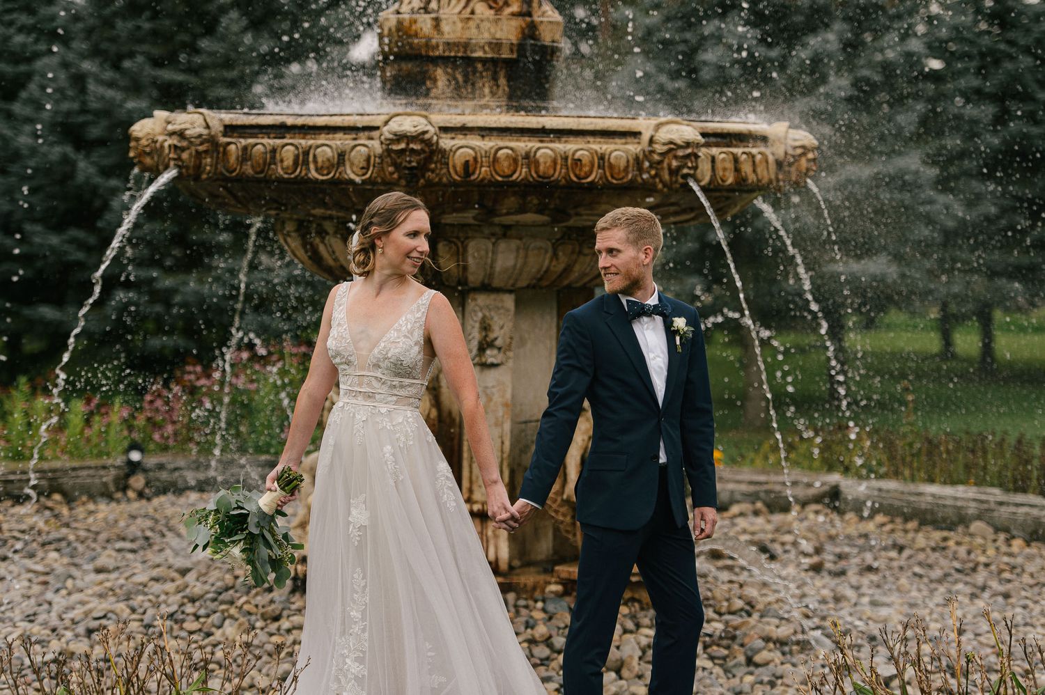 Couple shares intimate moments near a rustic stone fountain in a garden setting.