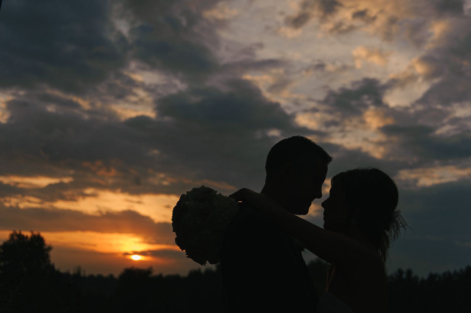 Silhouetted couple embracing against a dramatic sunset sky with clouds.