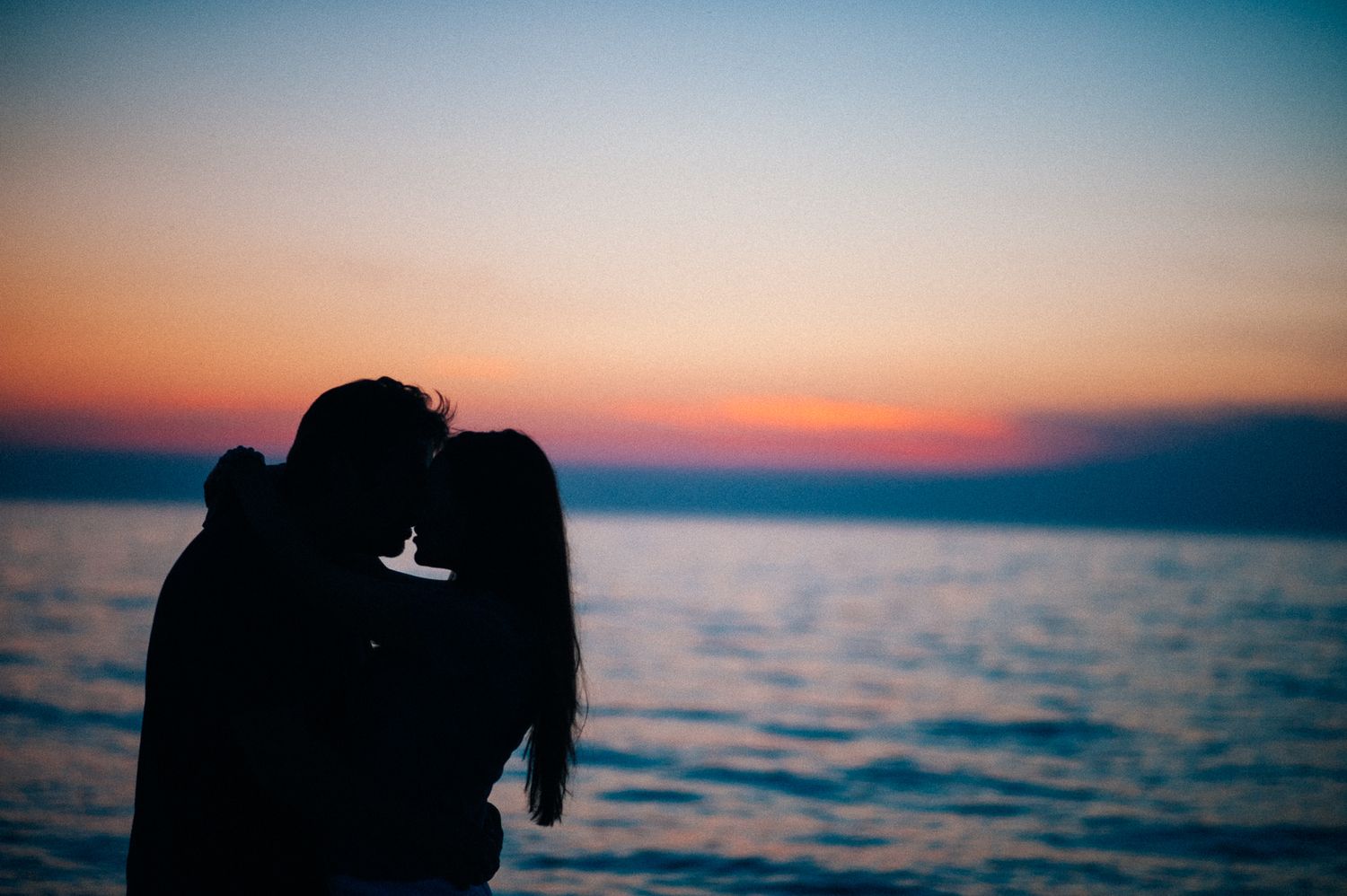 Silhouetted figures embracing against a vibrant ocean sunset.