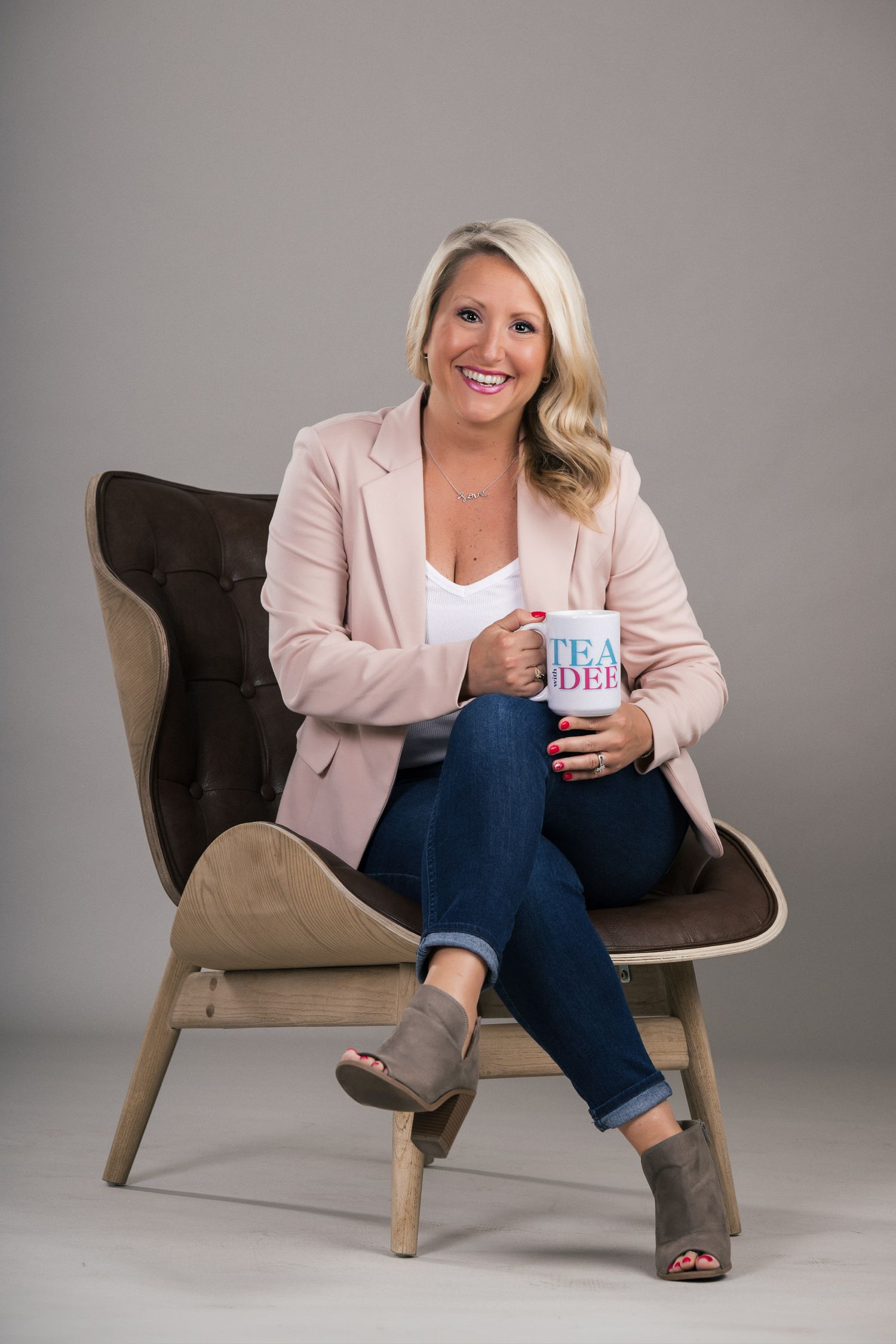 Professional lifestyle photos show someone seated in a brown armchair wearing a pink blazer and jeans while holding a coffee cup.