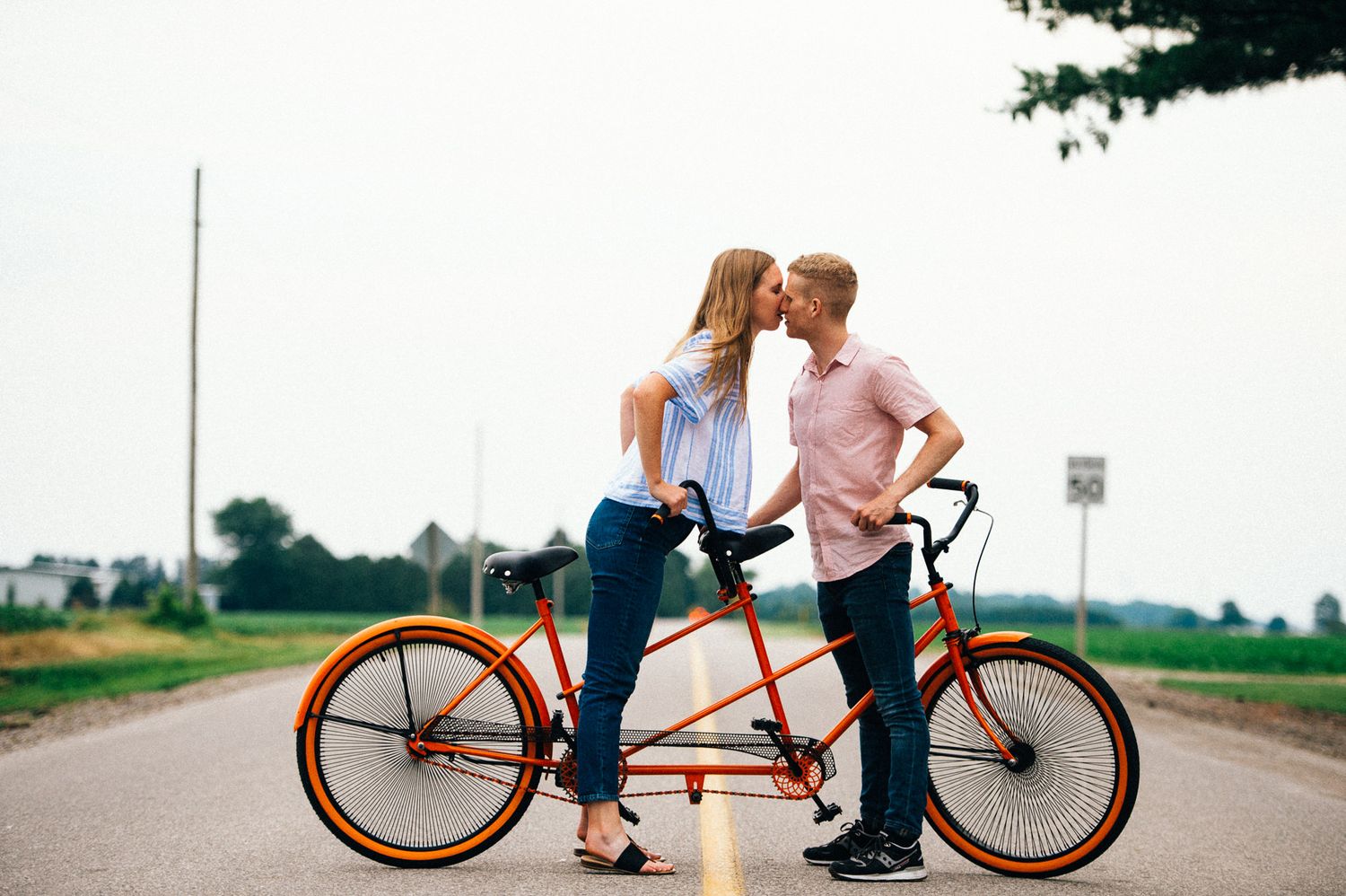 Couple riding together on an orange tandem bicycle on a rural road.