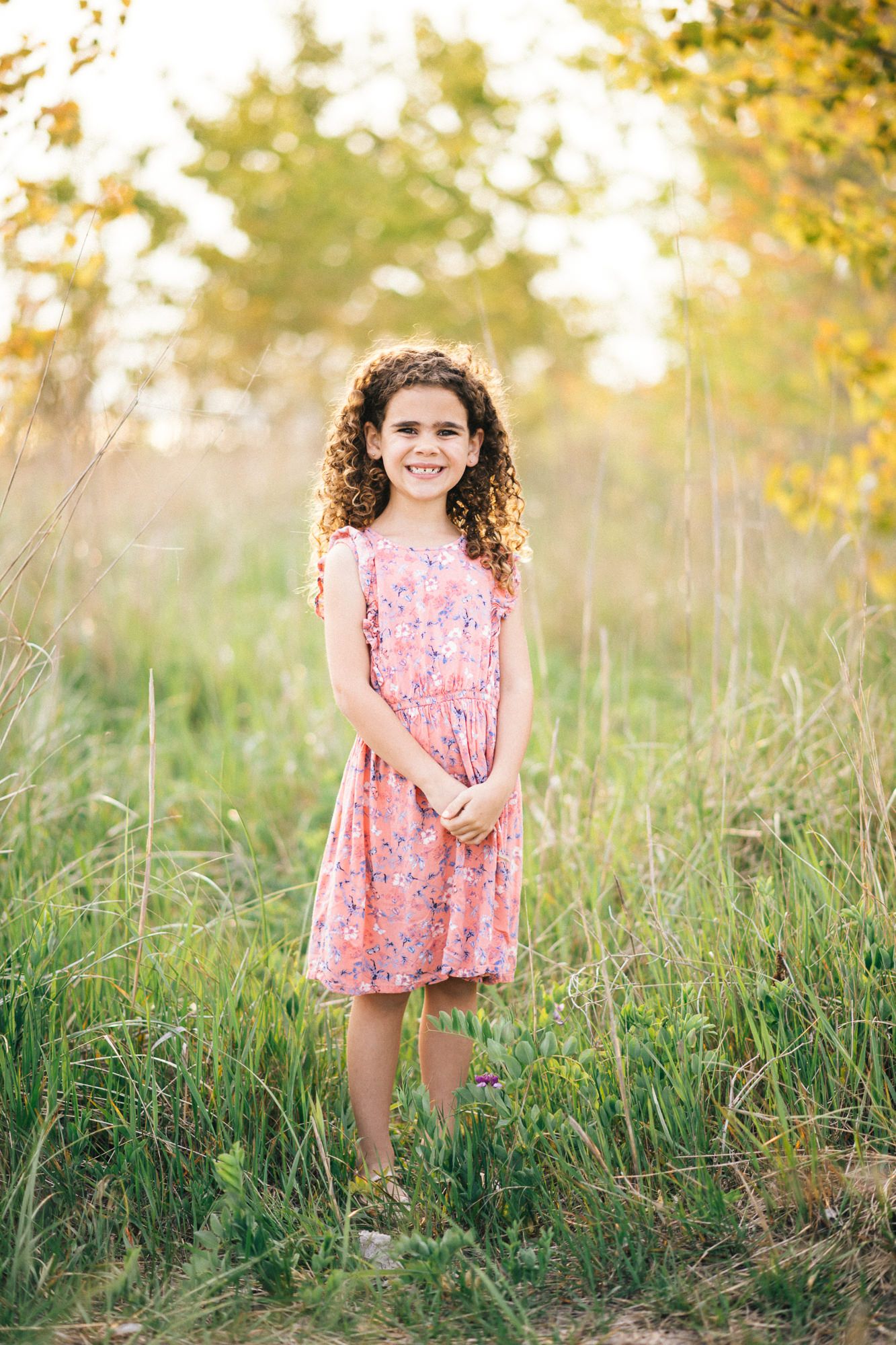 Young child in a pink floral dress playing in a grassy field during golden hour.