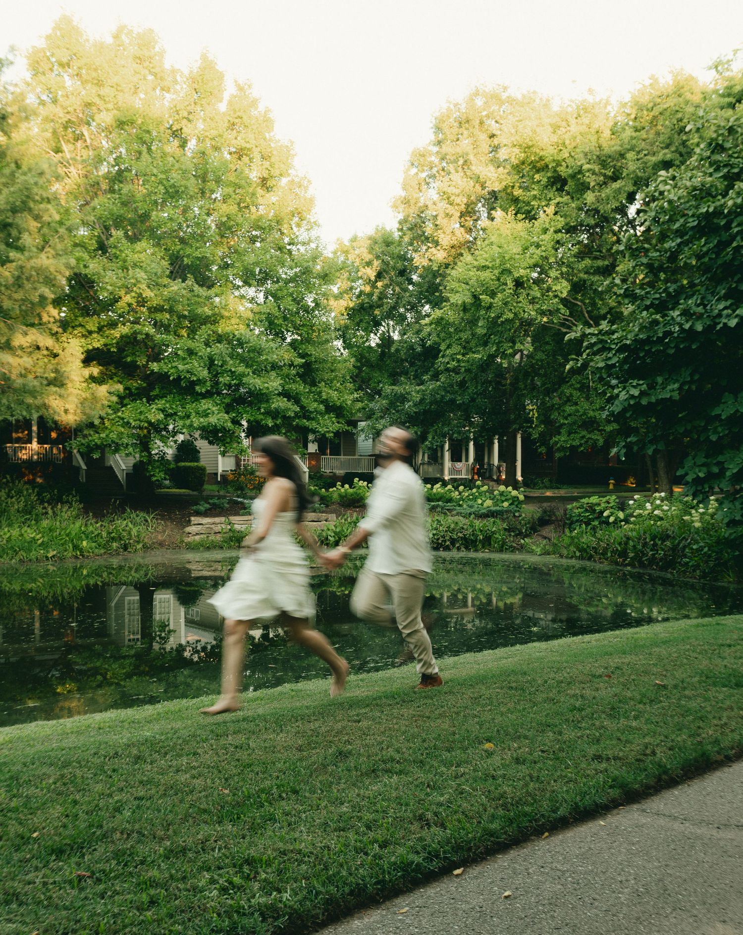 Blurred motion of couple running hand in hand past a serene garden pond.