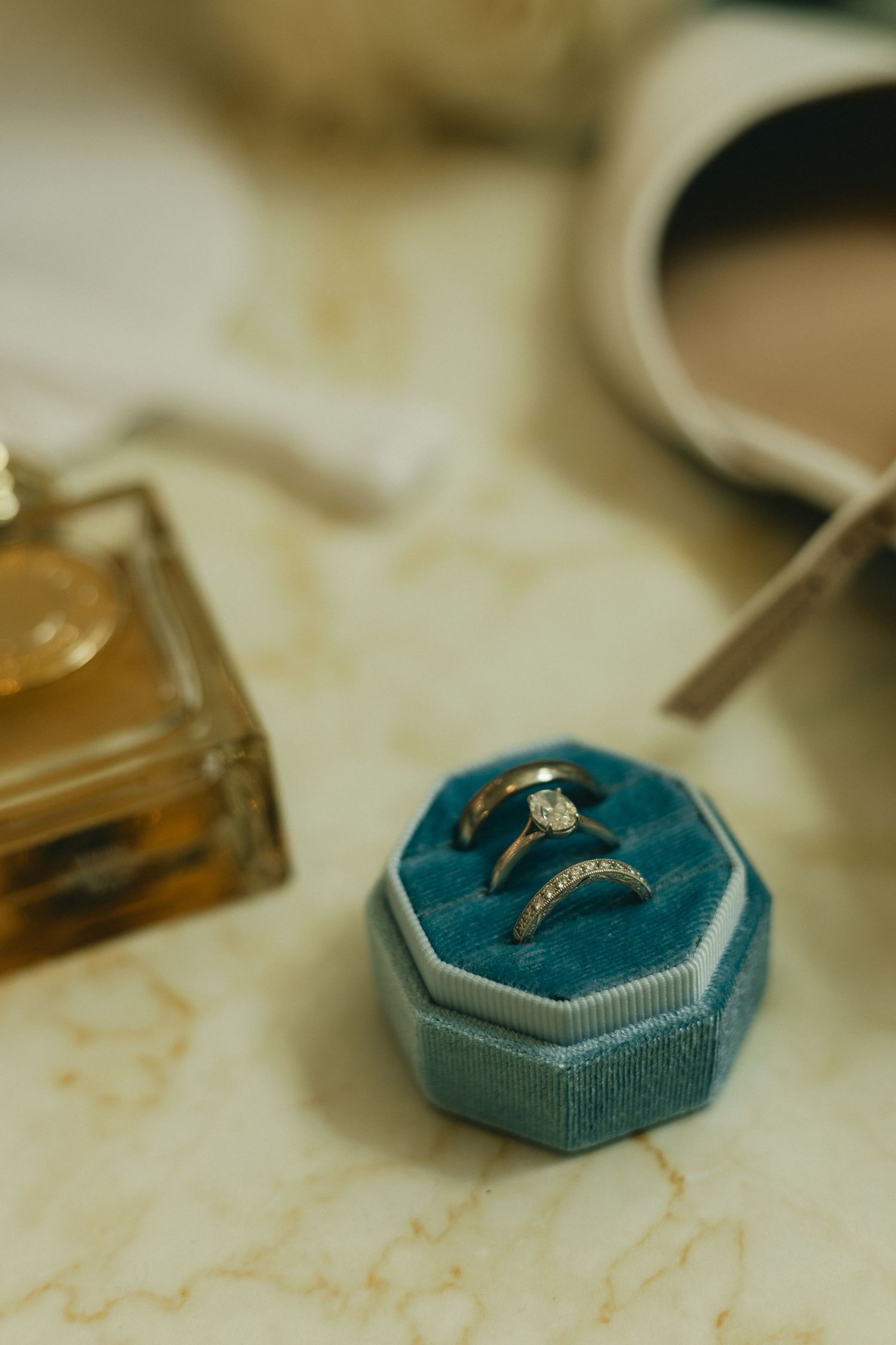Two gold wedding rings displayed in blue velvet octagonal ring box on marble surface.