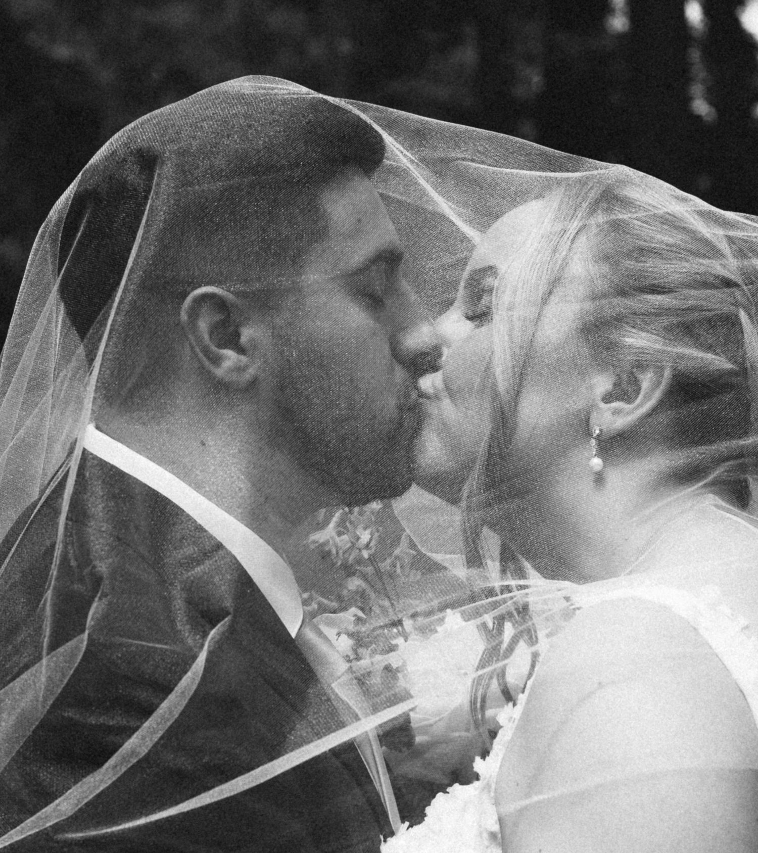 Black and white close-up of bride and groom sharing a romantic kiss beneath the bride's delicate veil.