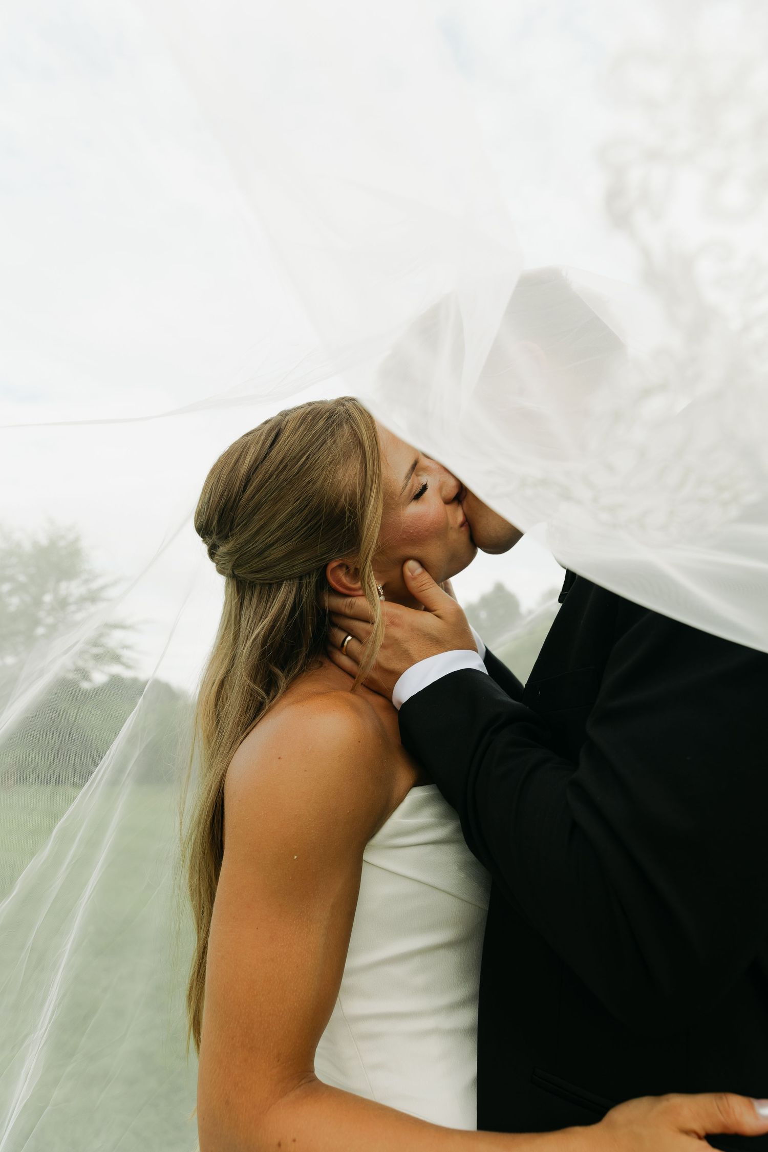 Bride and groom sharing a romantic kiss under a flowing white veil on their wedding day.