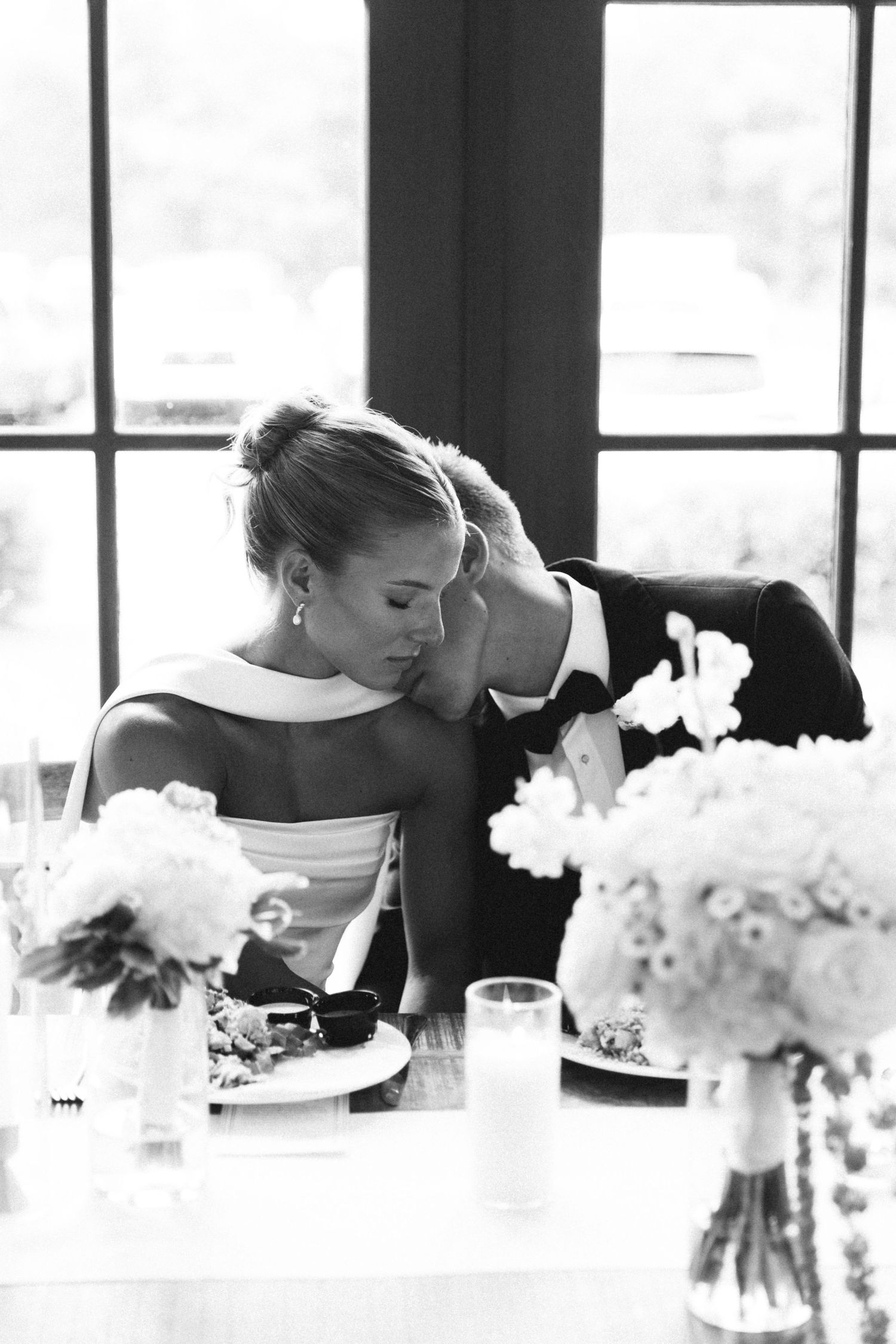 Black and white photo of bride and groom sharing an intimate moment at reception table.