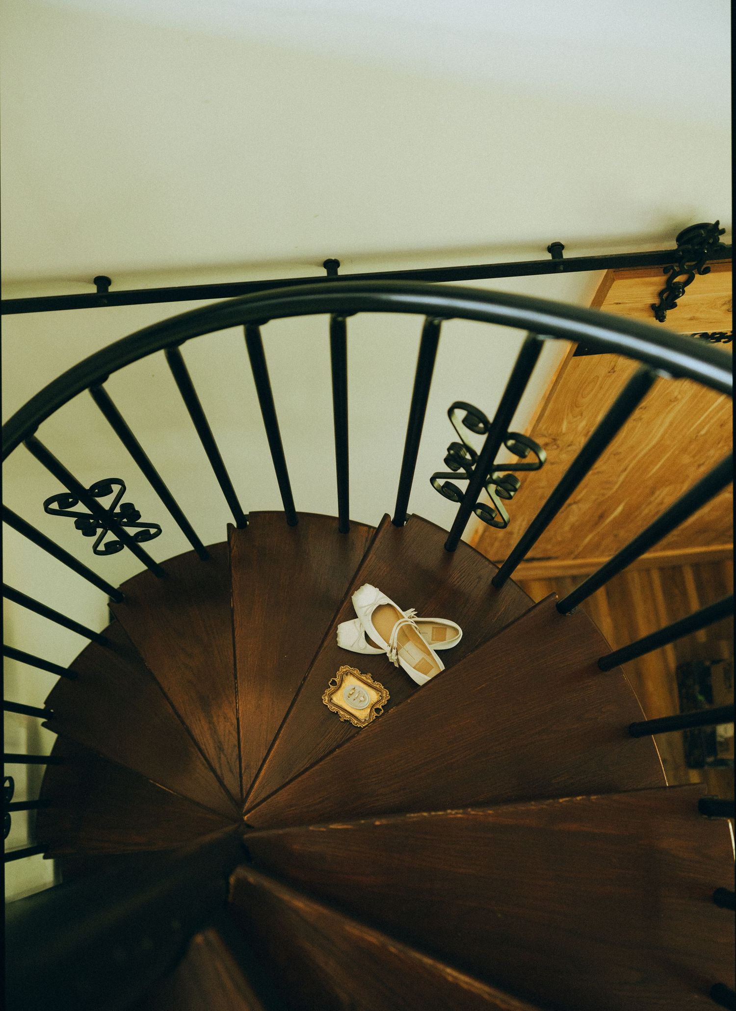 Elegant spiral staircase with black iron railing, wooden steps, and white bridal shoes placed on a step.