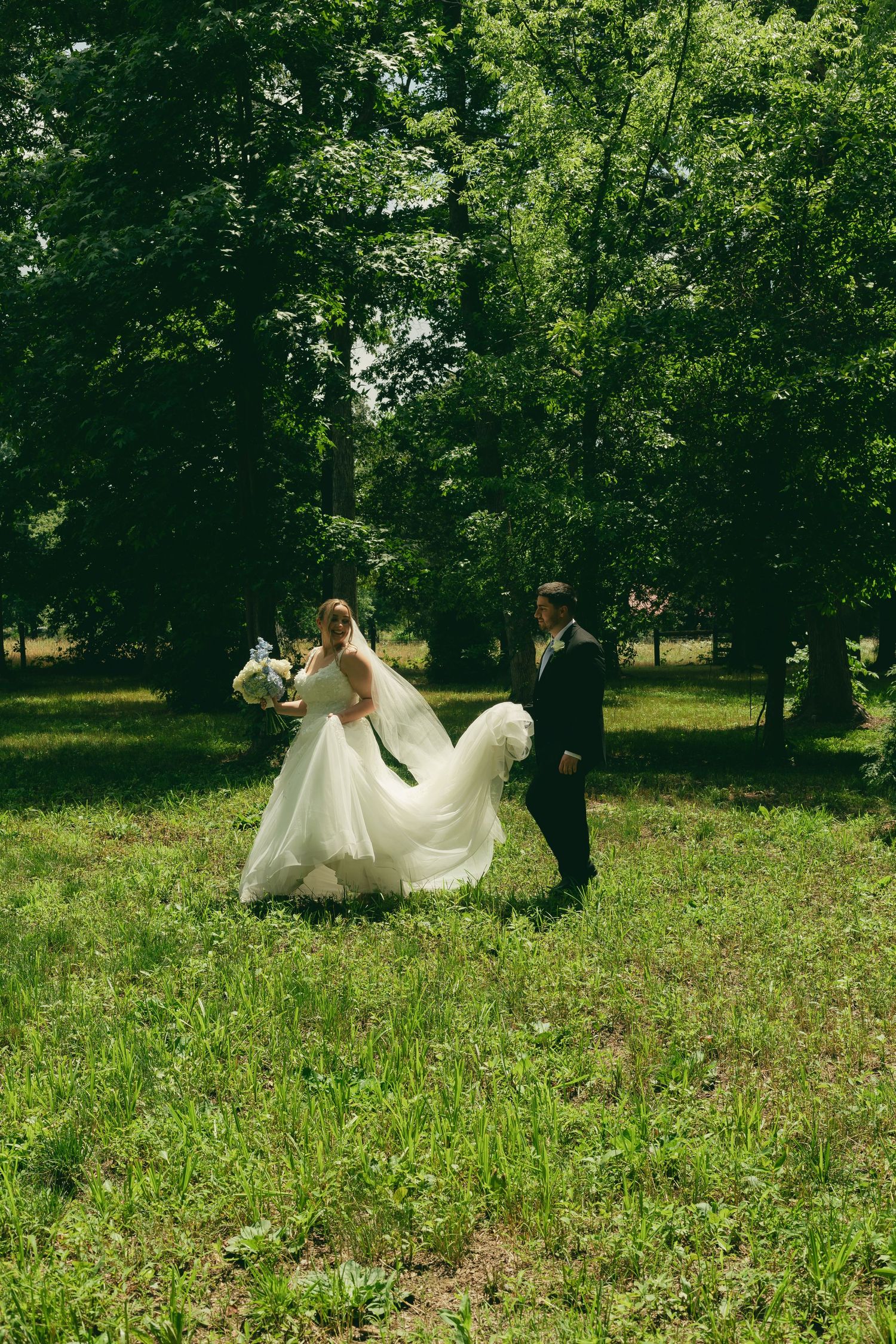 Bride and groom walk through a lush green forest, bride's gown flowing in the breeze.