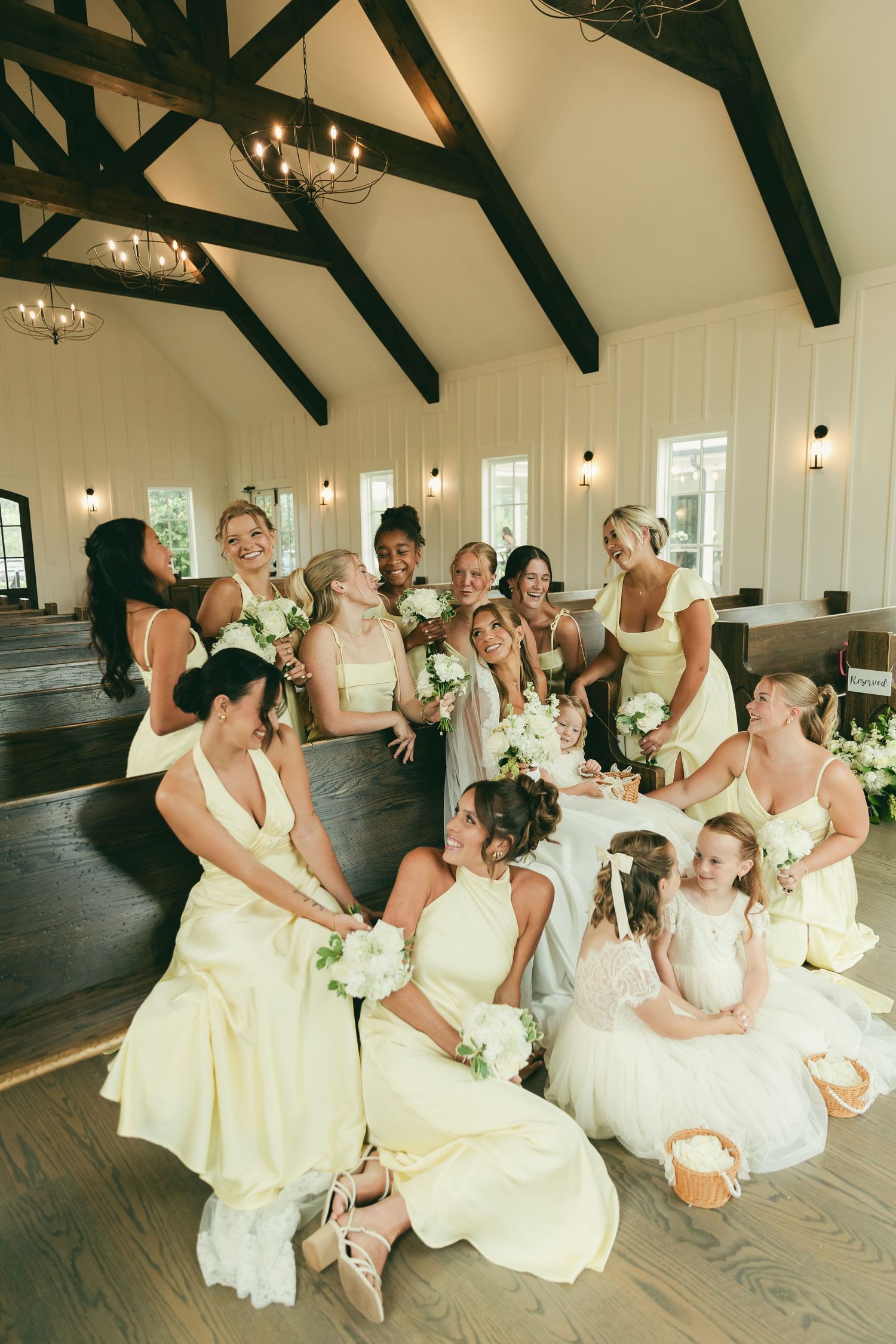 Bride and bridesmaids in pale yellow gowns laugh together inside a charming chapel venue.