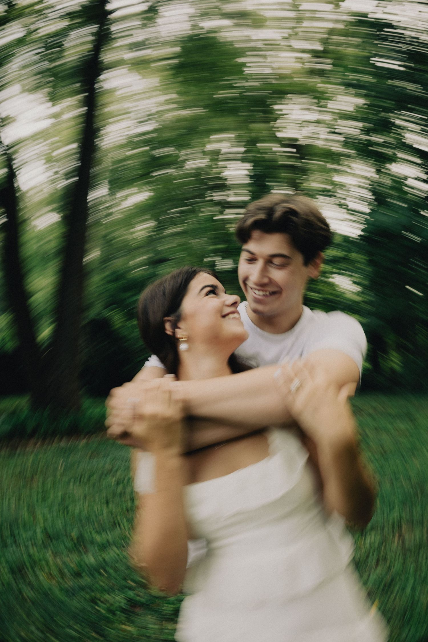 A joyful couple embraces and spins together in a green forest, captured with a radial blur effect.