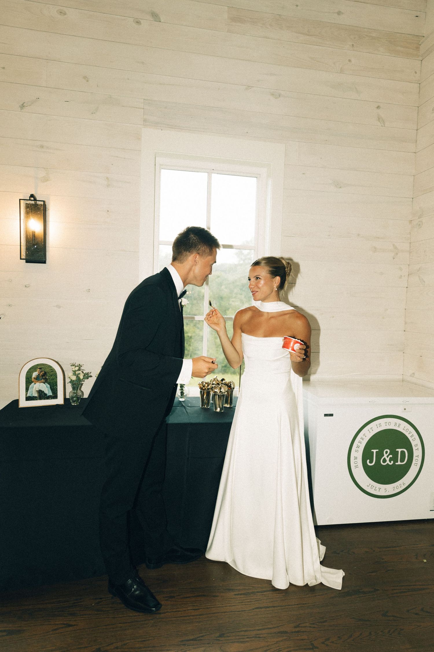 Bride and groom laugh together while cutting their wedding cake at indoor reception venue.