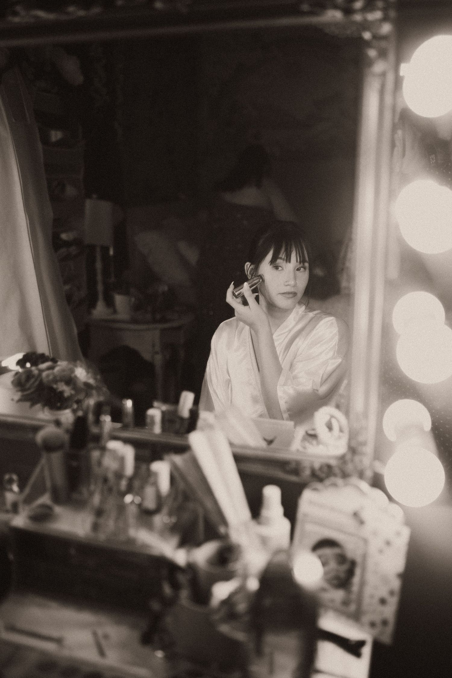 Vintage black and white photo of bride applying perfume at vanity mirror with Hollywood lights.