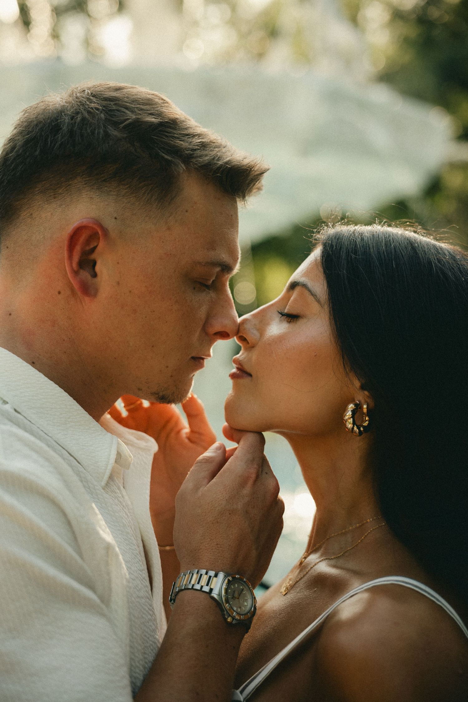 Romantic couple almost kissing in golden sunlight during outdoor engagement photo session.