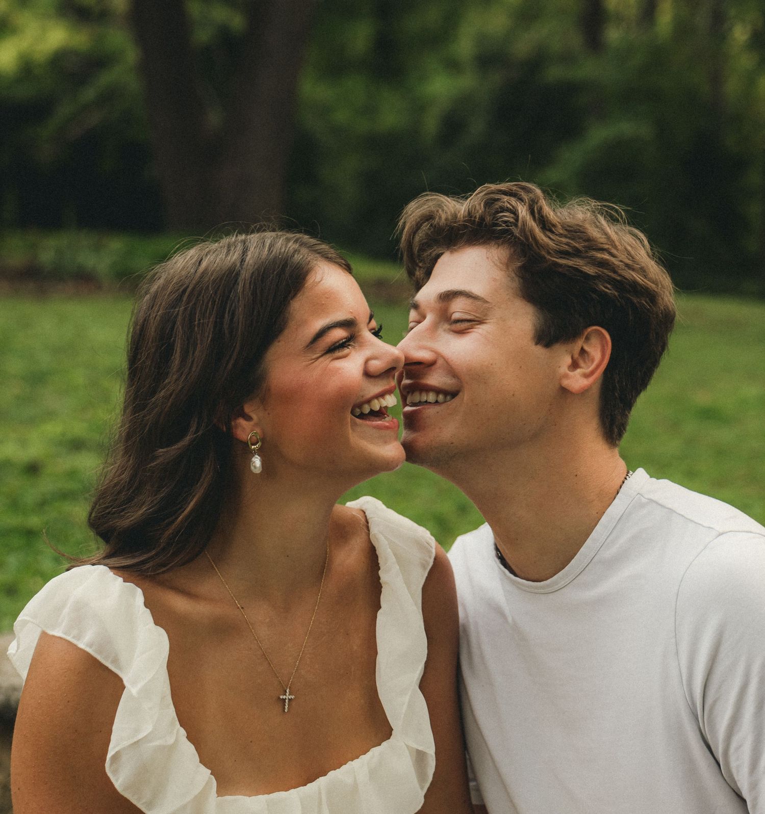 Happy young couple sharing a joyful moment outdoors, laughing and almost kissing in a green park.