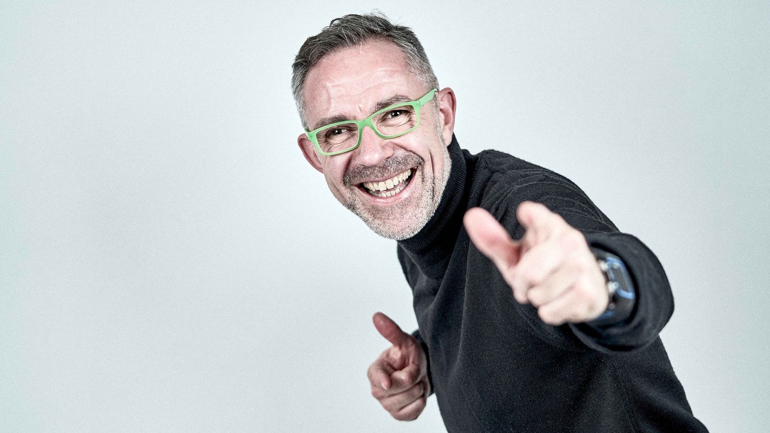 Energetic portrait of someone in black sweater giving thumbs up gesture against light background.