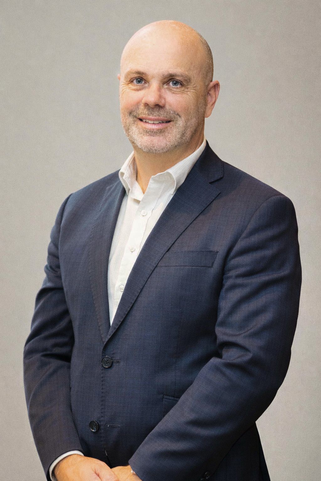 Professional headshot of person in navy suit and white shirt against neutral gray background.