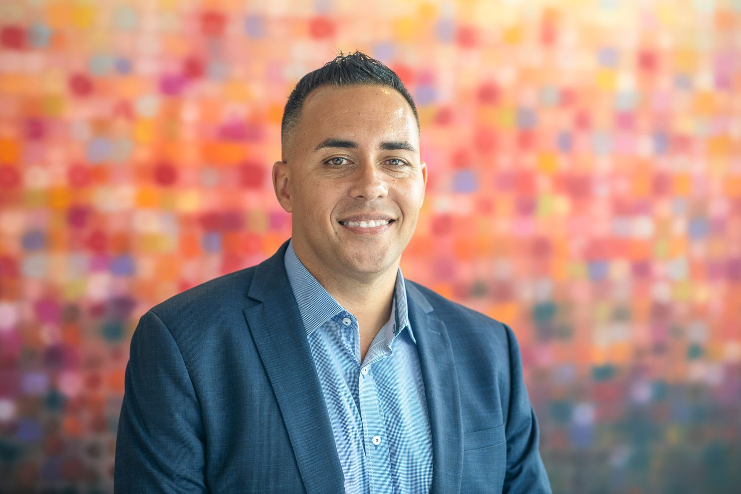 Professional headshot of a man in blue suit against colorful abstract background.