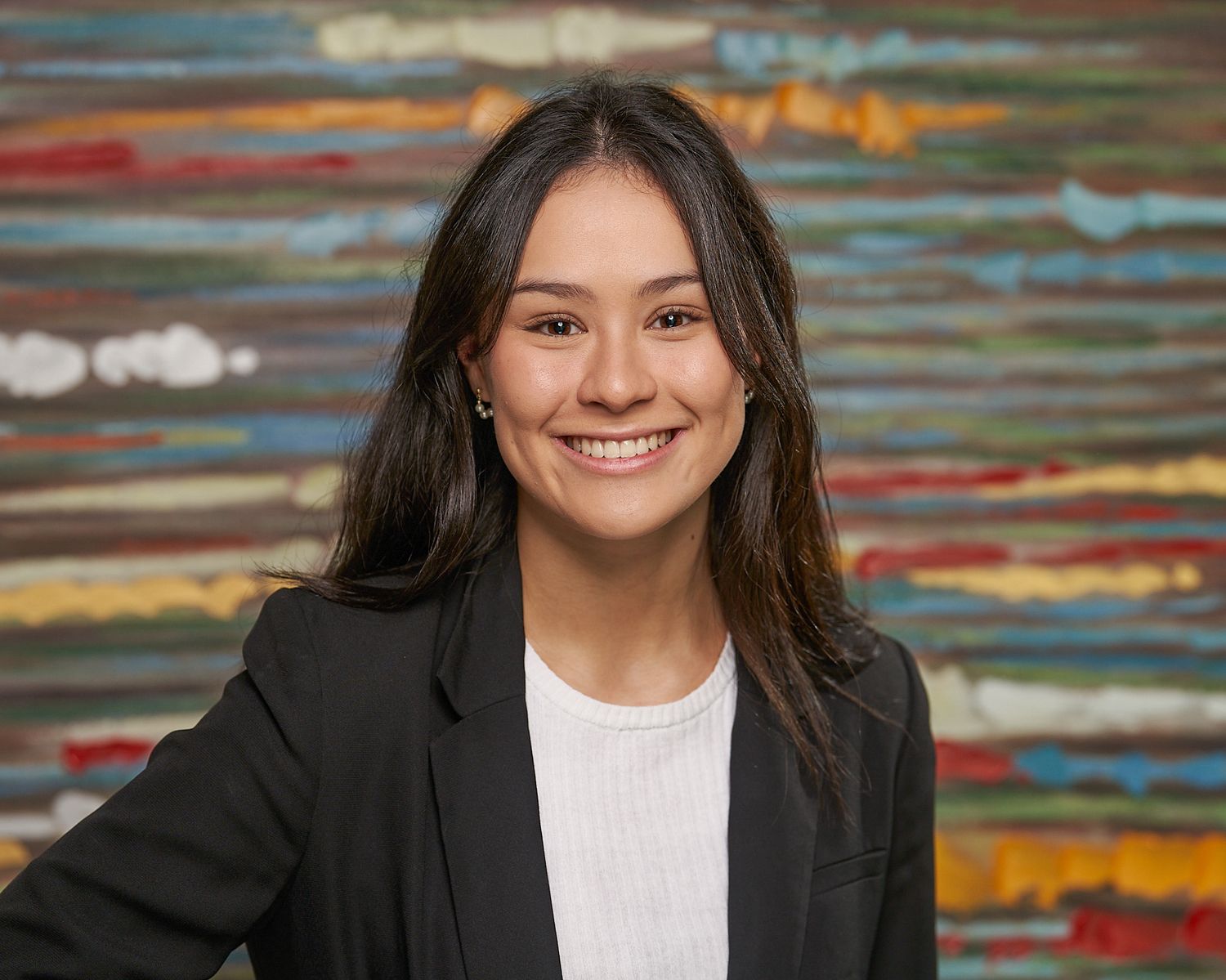 Professional headshot against colorful striped background wearing black blazer and white top.