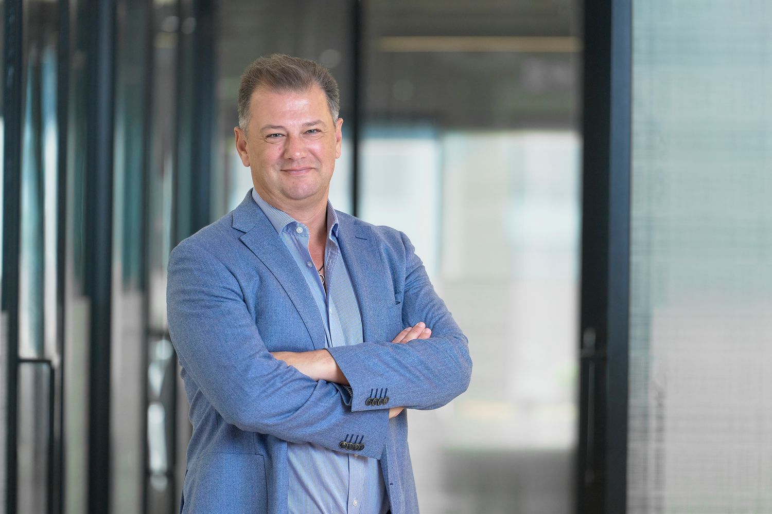 Business headshot of a man in suit  posing in corporate office setting with glass walls.