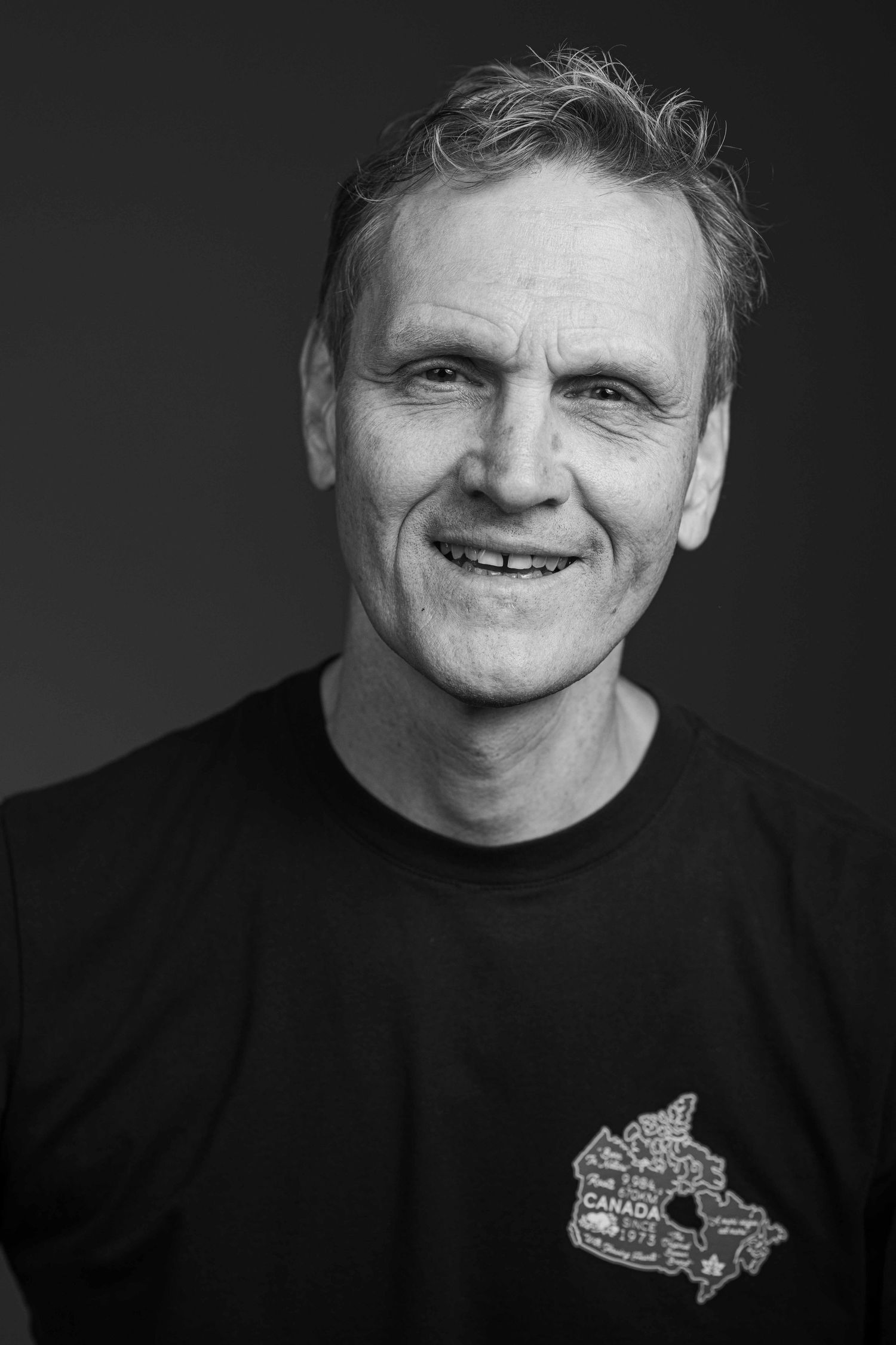 Black and white portrait of a smiling person wearing a black t-shirt with a Canadian maple leaf design.