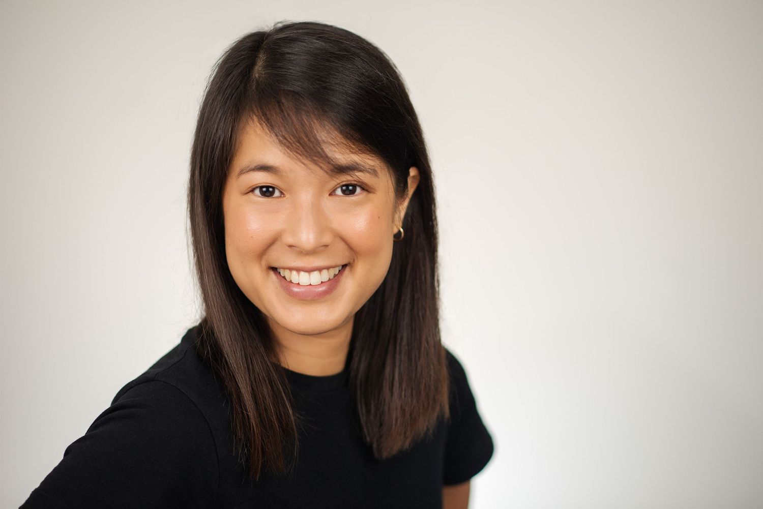 Professional headshot of someone with long dark hair wearing a black sweater against a light background, smiling warmly.