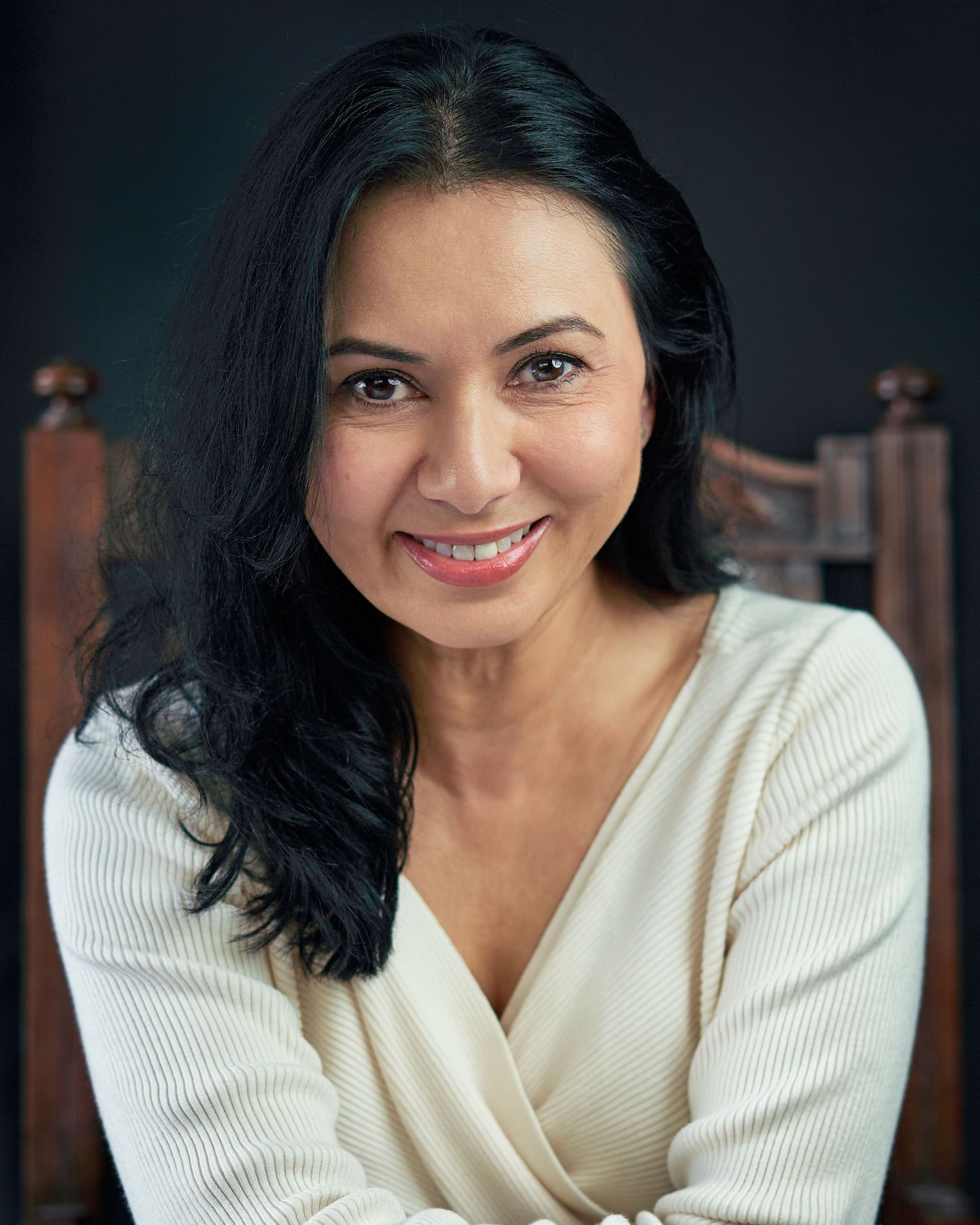 Portrait featuring a woman with a warm expressions in cream sweater against dark background.