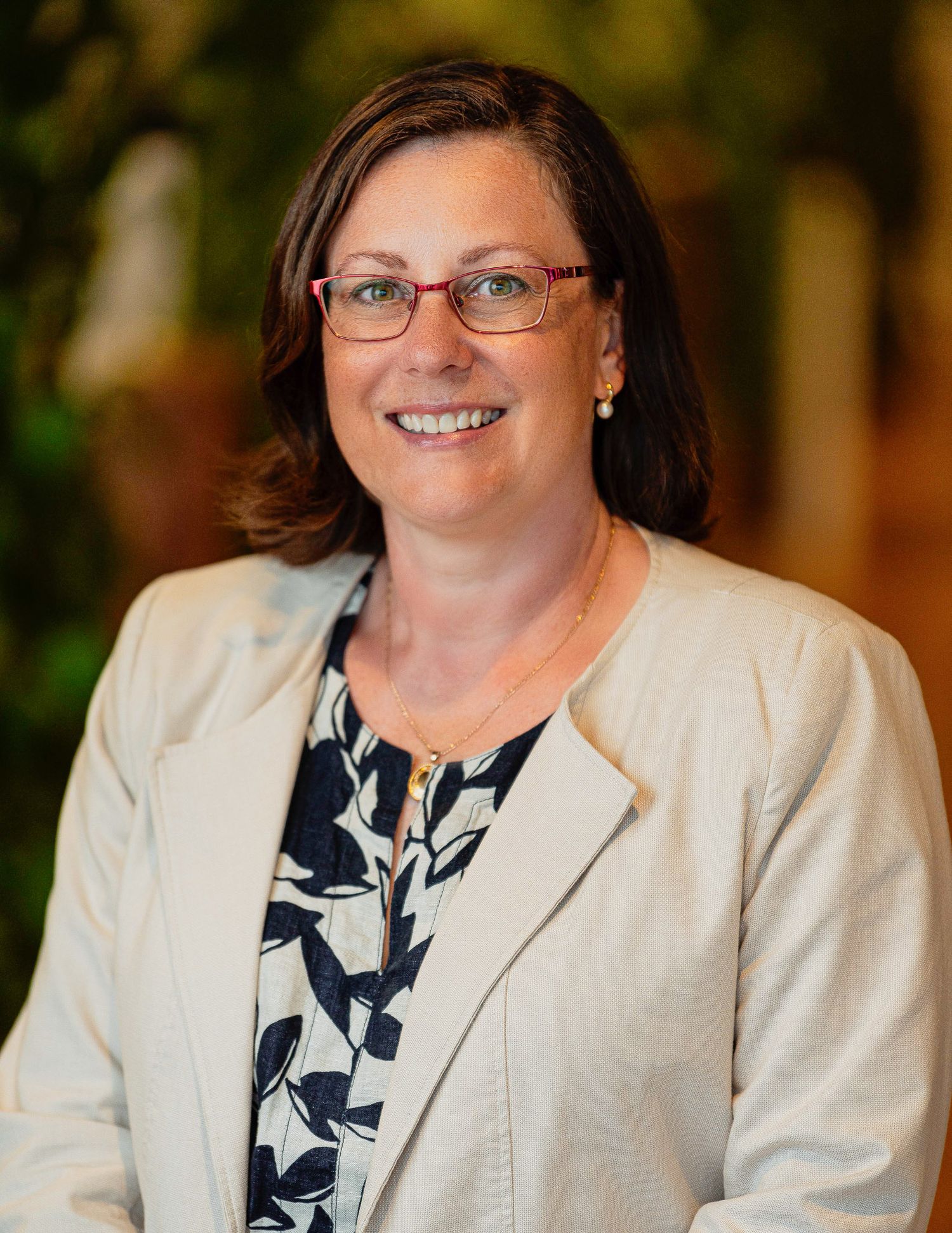 Professional portrait headshot of a woman in cream blazer and floral print blouse against warm background.