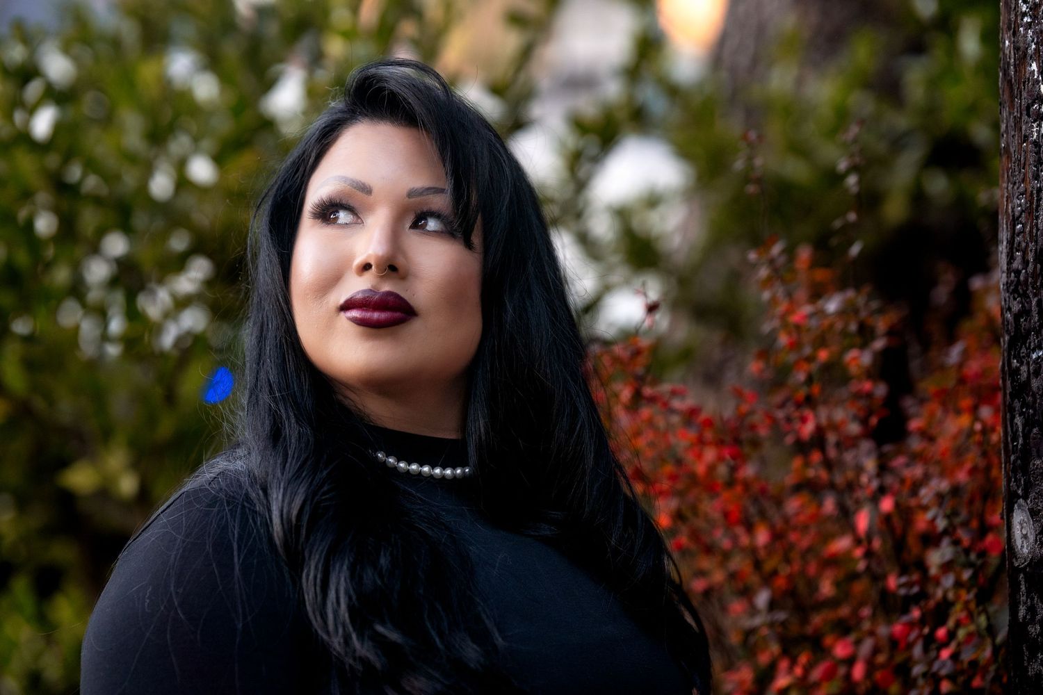 Portrait of woman in black sweater with red lipstick against fall foliage.