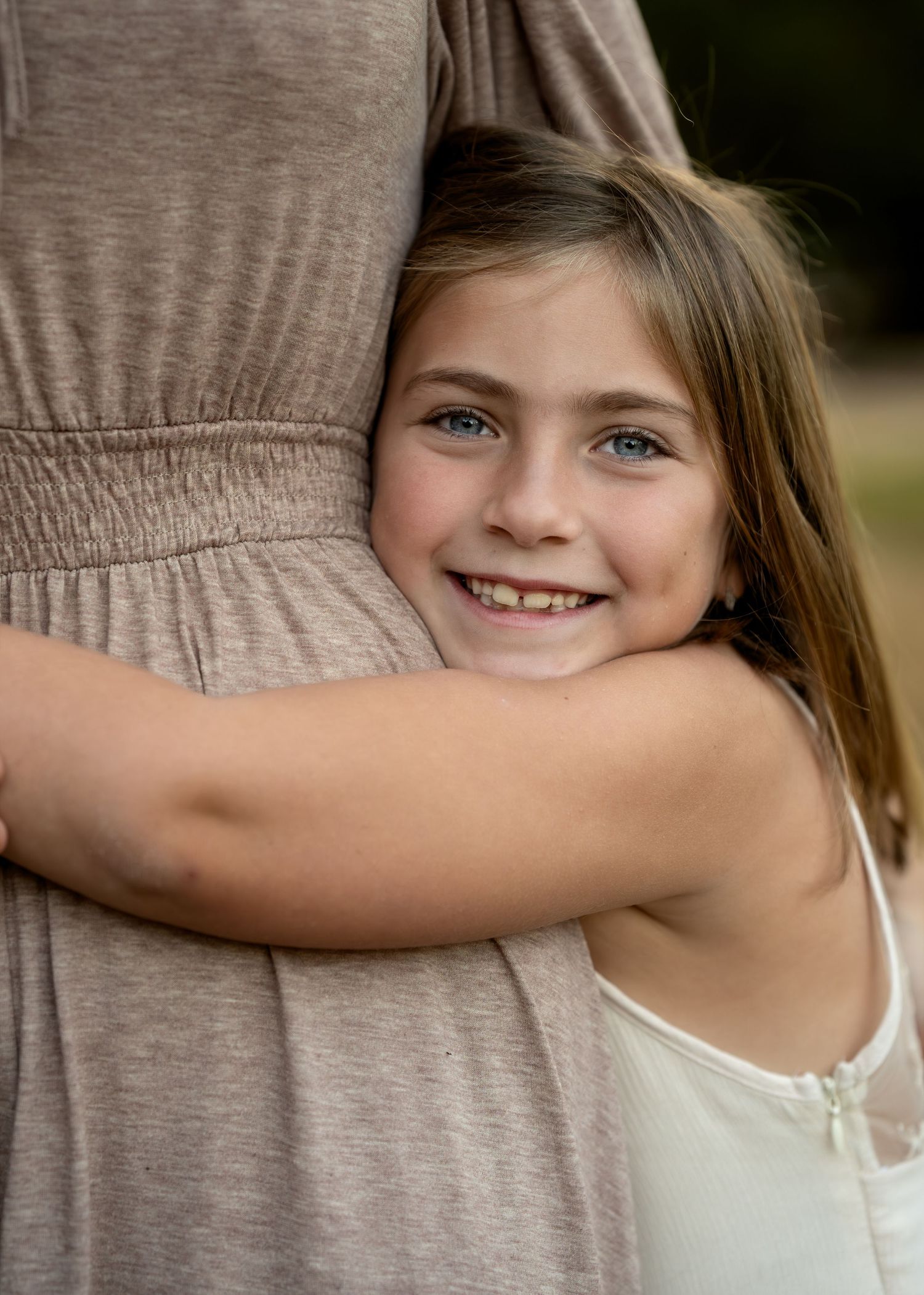 Child in white tank top hugging someone wearing a grey shirt in a candid moment.