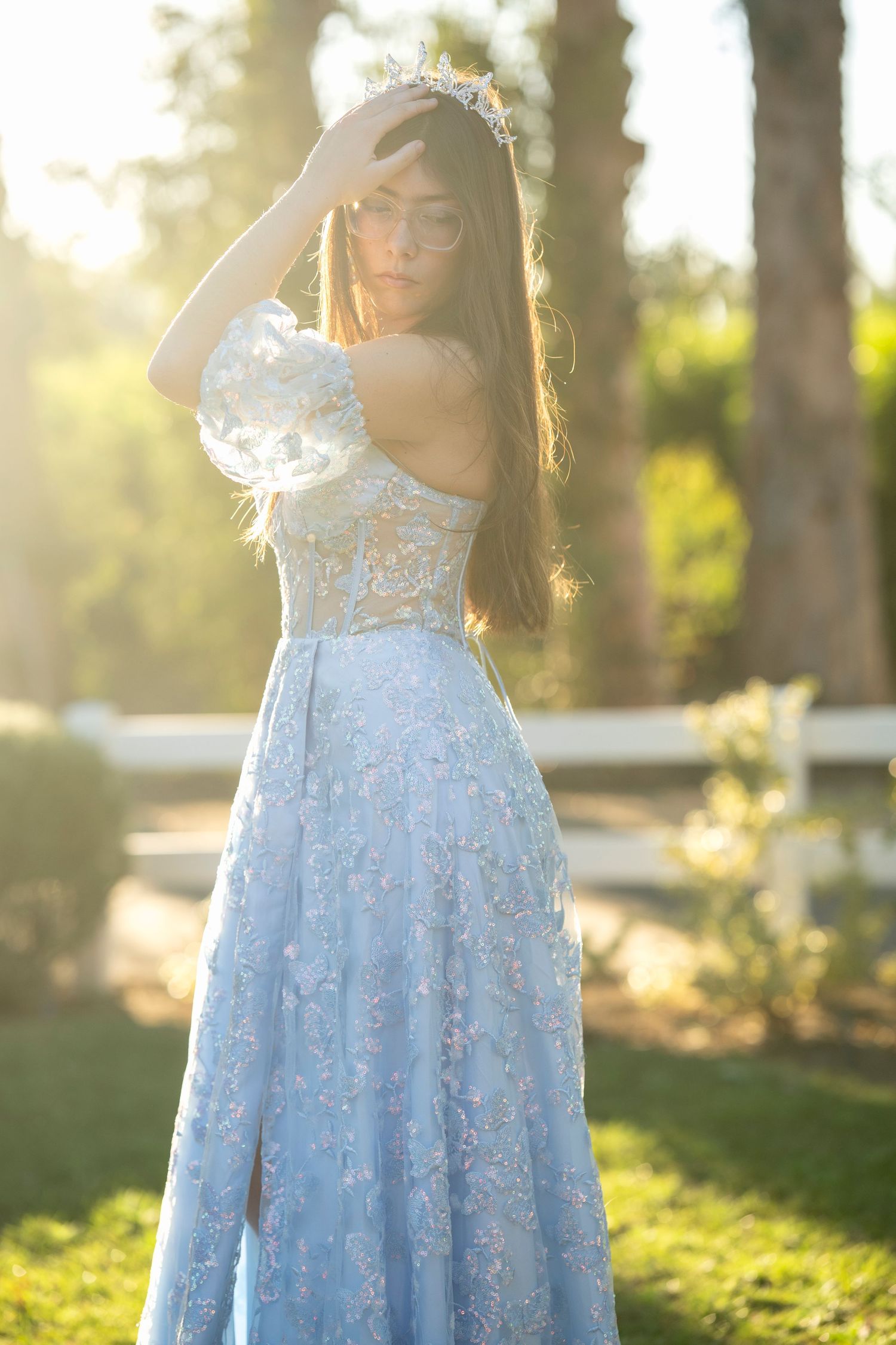 A dreamy portrait in a light blue lace gown with sunlit forest backdrop during golden hour.