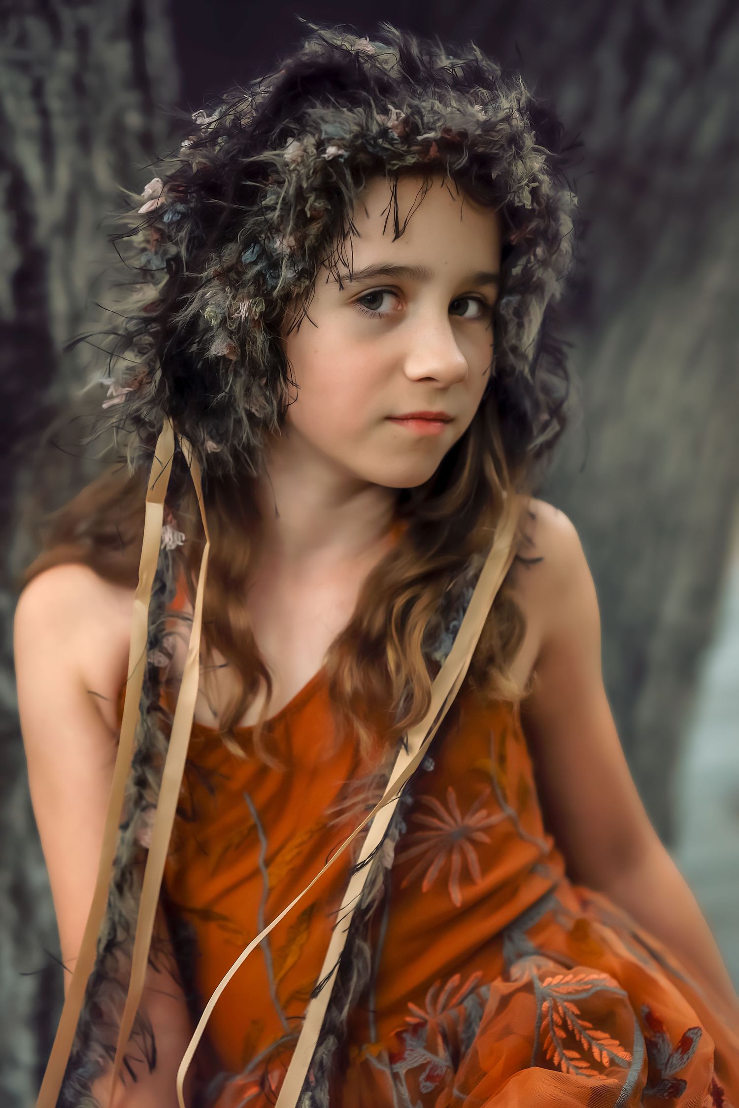 Figure in an orange dress and feathered headdress poses in a whimsical woodland photoshoot.