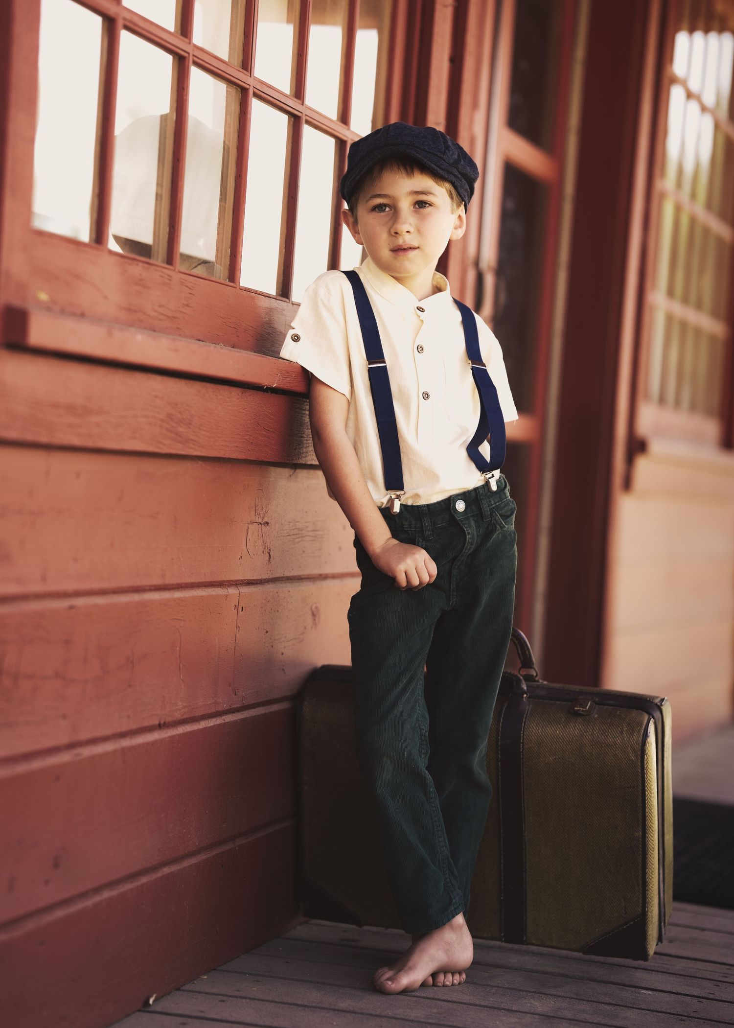 Vintage-styled scene with suspenders and classic suitcase on wooden porch.