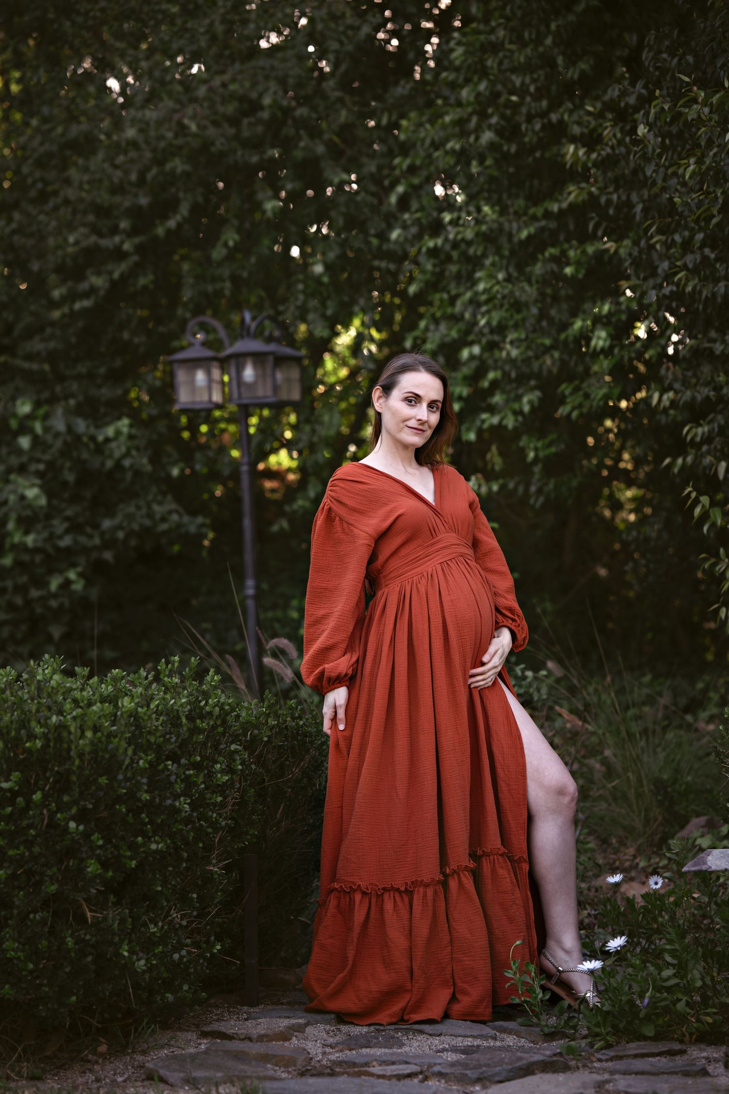 A flowing rust-colored dress is captured in a series of artistic outdoor poses against a backdrop of lush greenery.