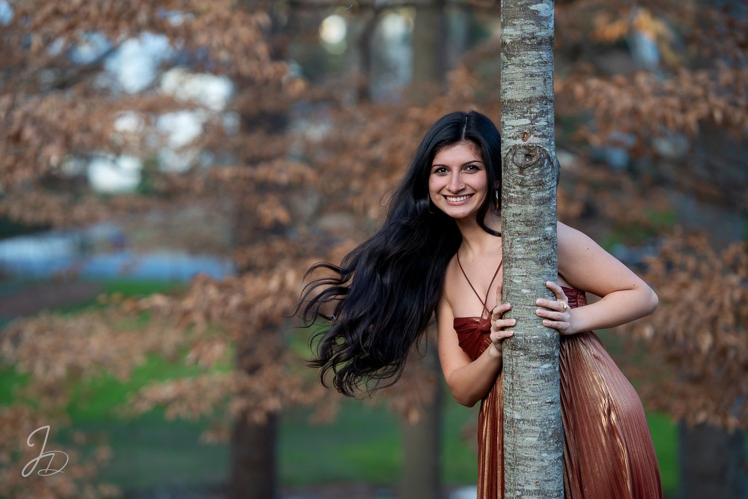 Outdoor photoshoot with tree trunk and autumn leaves in background.