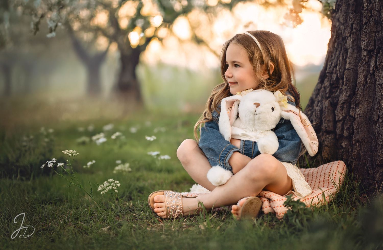 A figure sits under a tree with a stuffed bunny companion during springtime.