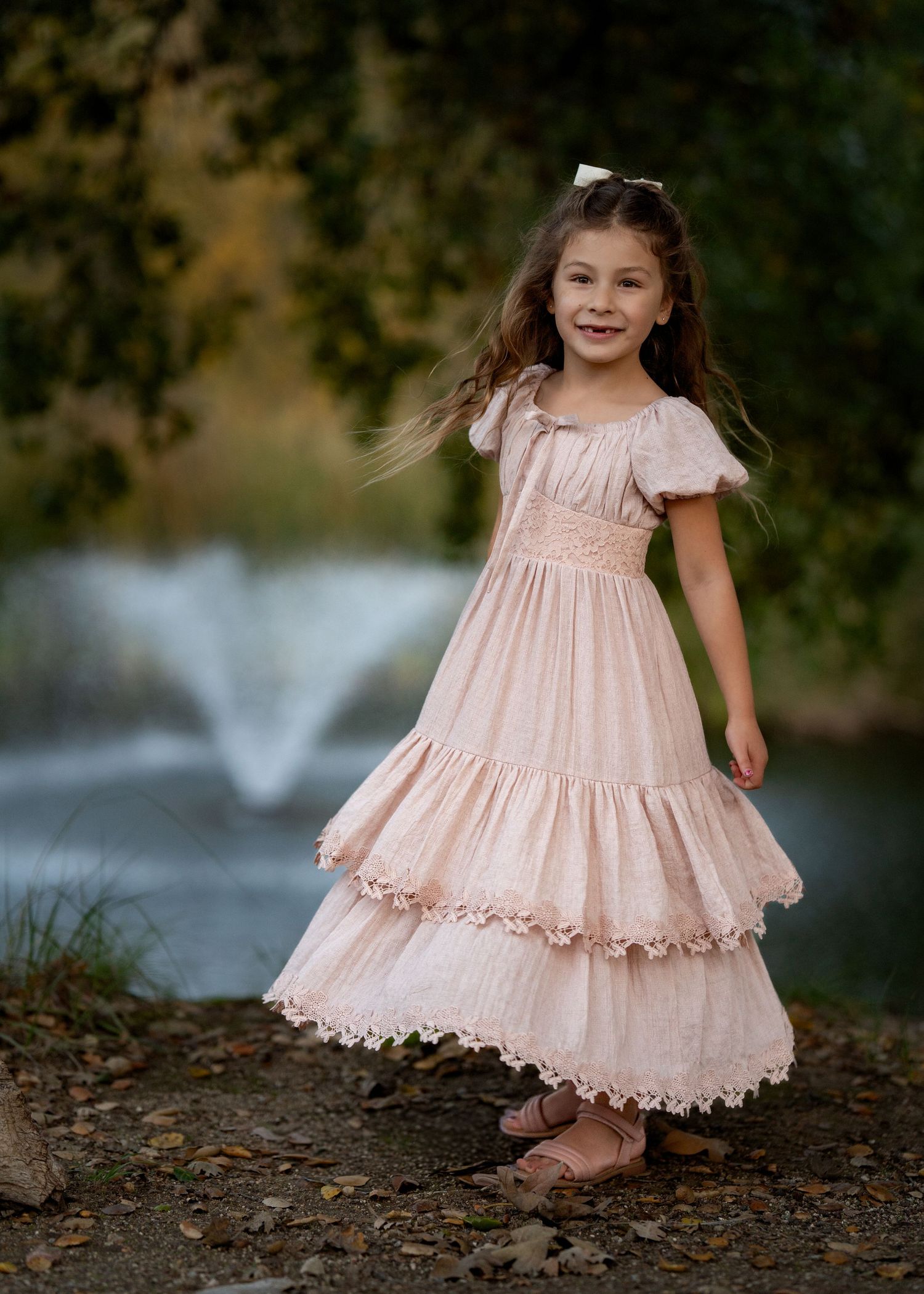 A flowing pink dress twirls gracefully near a fountain in an autumn garden setting.