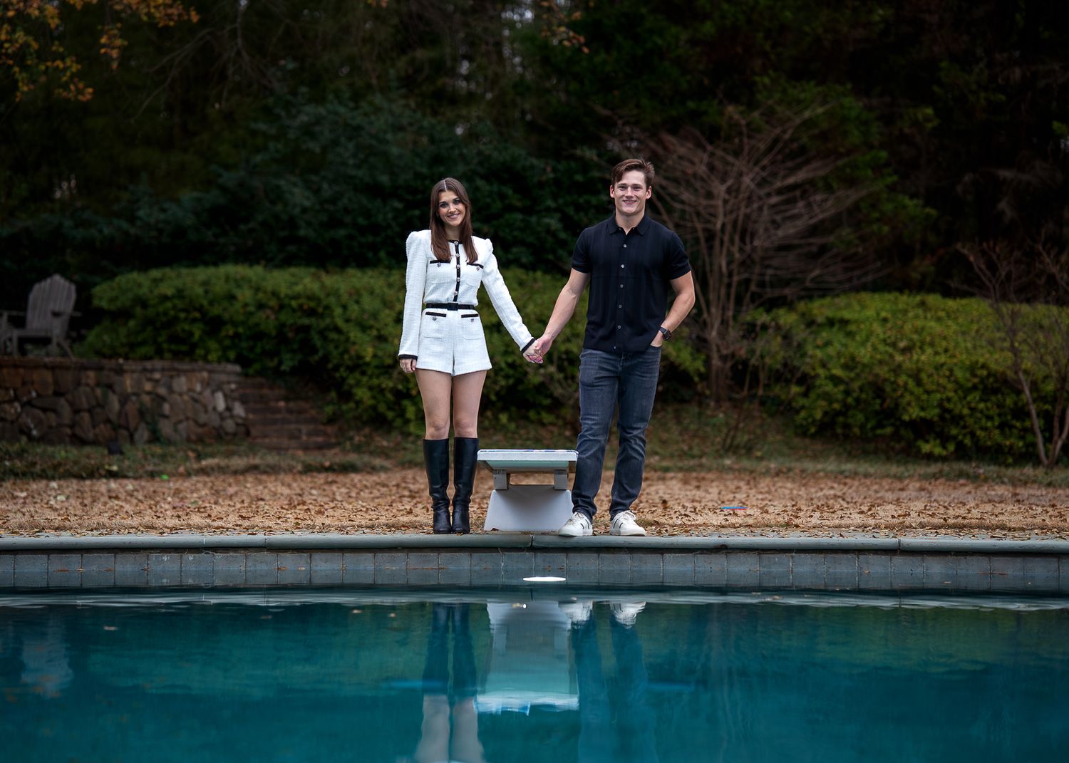 Couple sitting at edge of serene pool surrounded by lush landscaping.