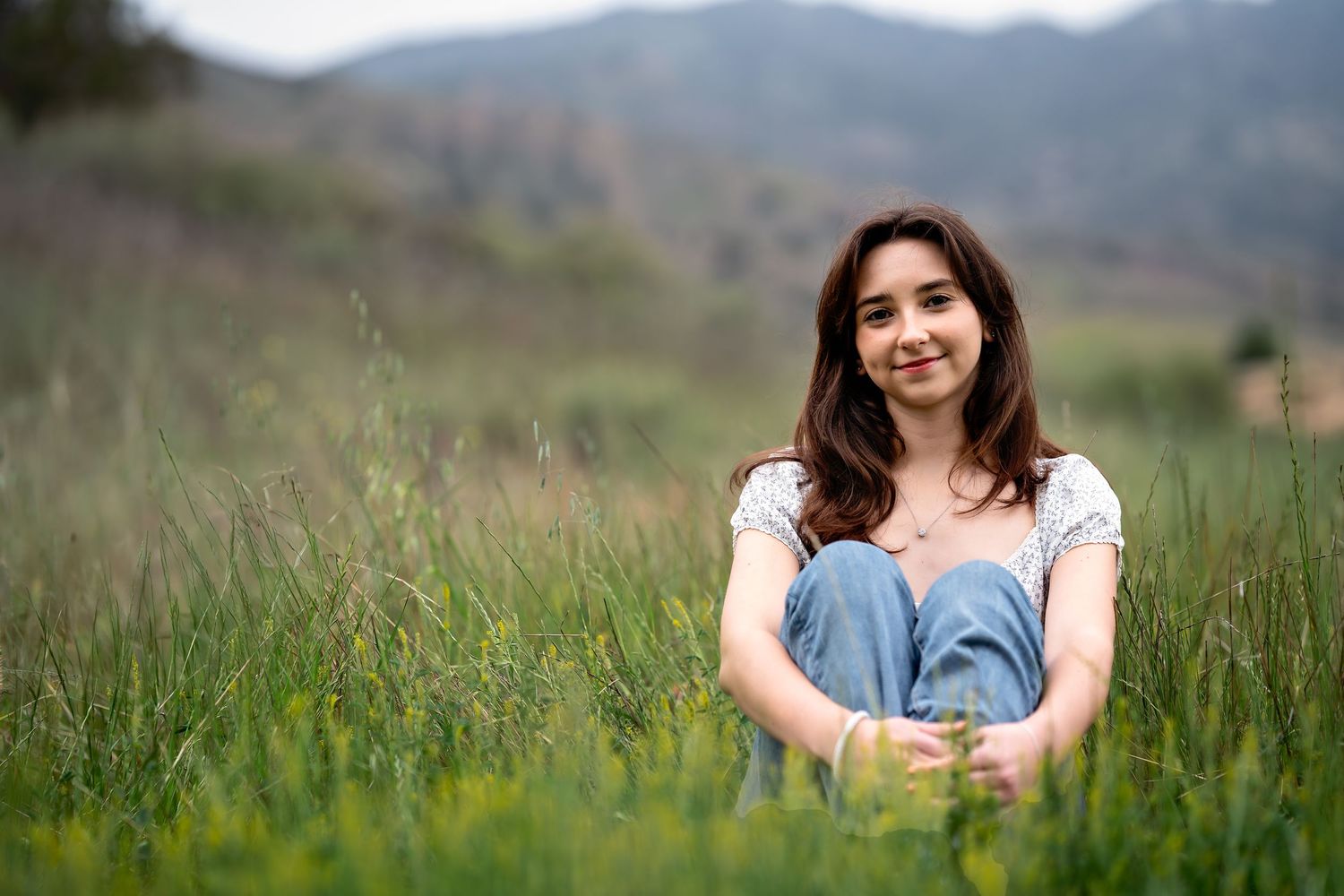 Someone sits peacefully in tall grass with mountains visible in the background on a sunny afternoon.