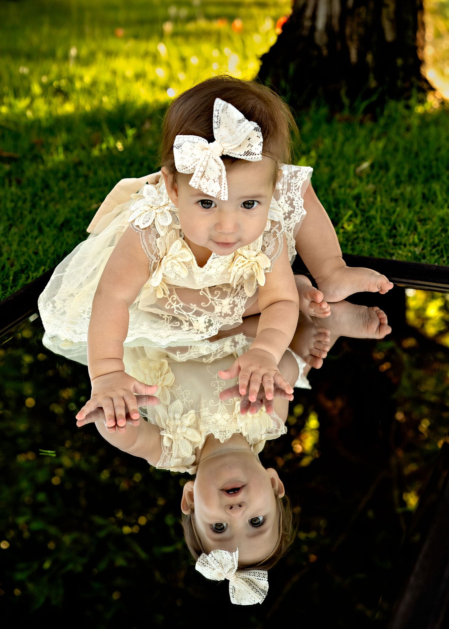 Sweet baby in white lace dress lying on grass during golden hour outdoor photoshoot.
