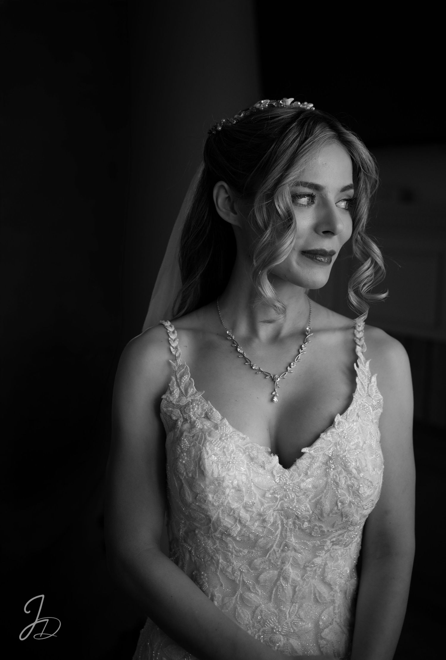 Black and white bridal portrait of elegant woman in lace wedding gown, tiara, veil, and diamond necklace.