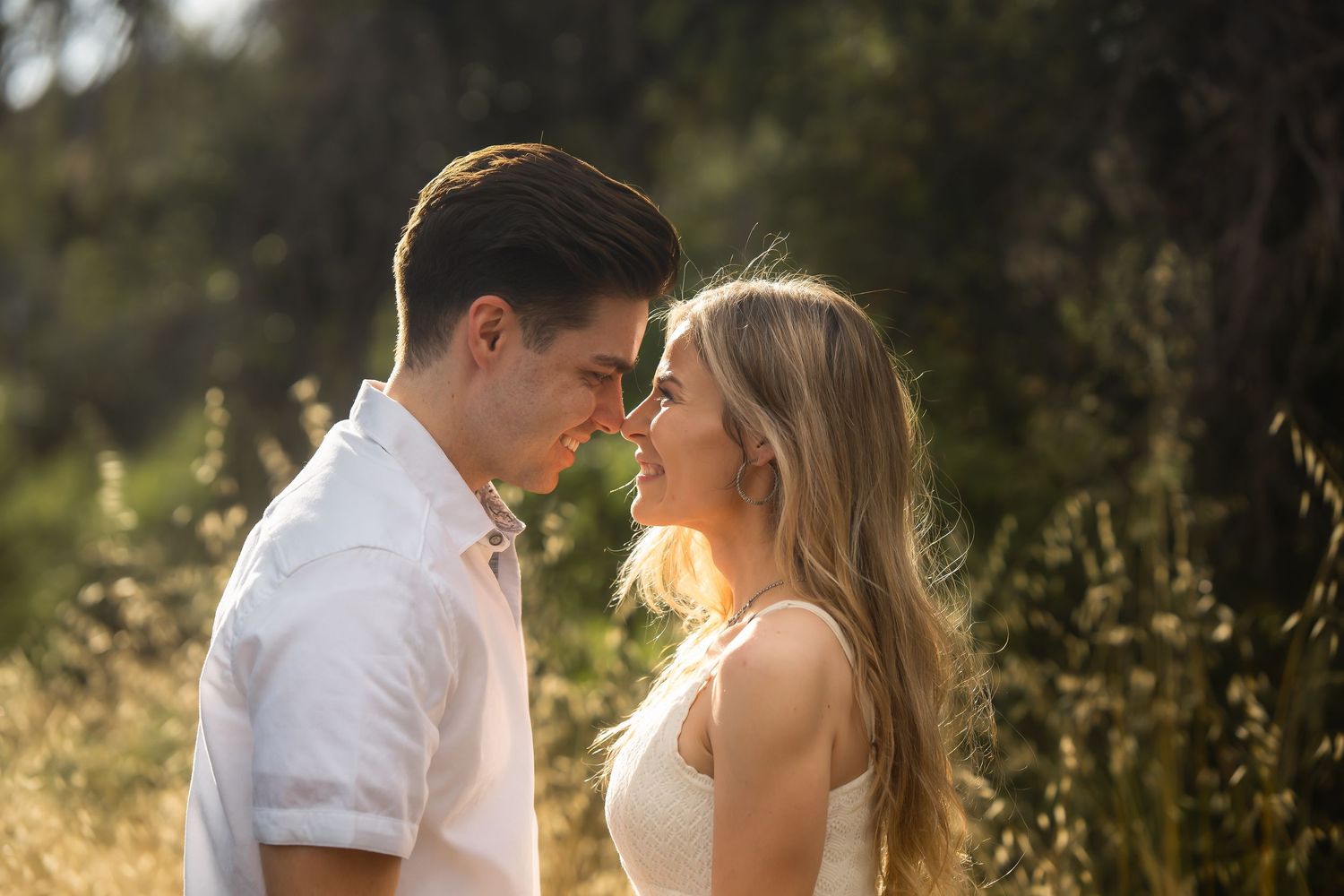 A young couple shares a romantic moment outdoors, smiling at each other in golden sunlight.