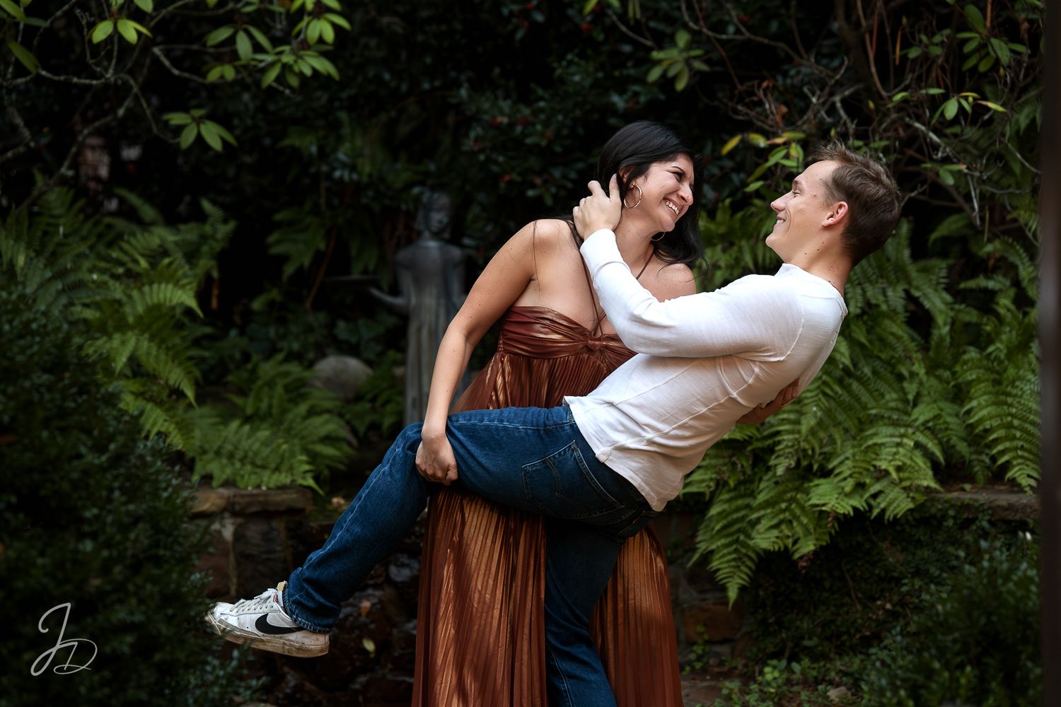 Romantic couple dancing playfully in a lush garden setting with ferns and greenery.