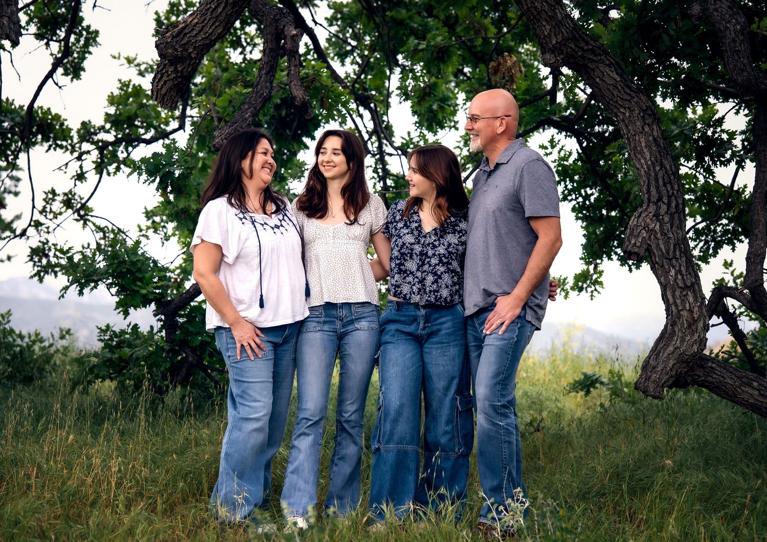 A group of people wearing jeans and casual clothing stand together outdoors on grassy terrain.
