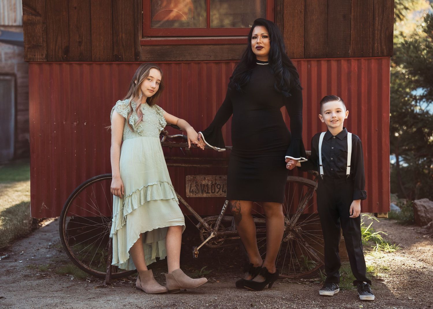 Three people pose together near a rustic red barn with an antique bicycle.