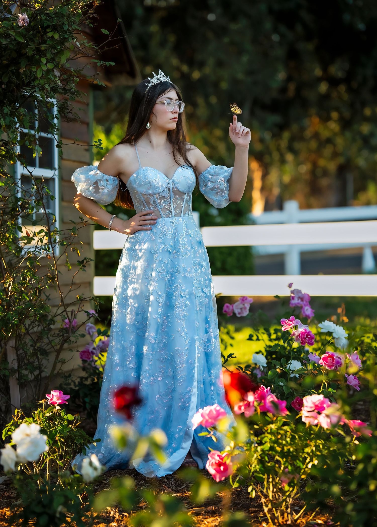 A light blue off-shoulder dress flows gracefully among vibrant garden flowers in an outdoor setting.