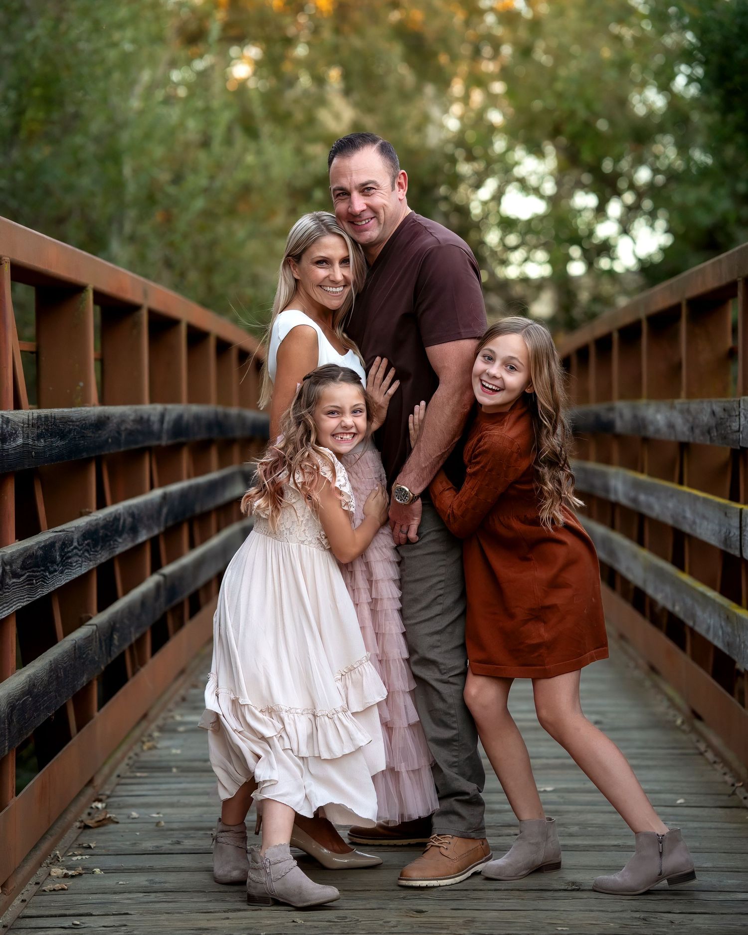 Family poses together on wooden bridge surrounded by autumn trees.