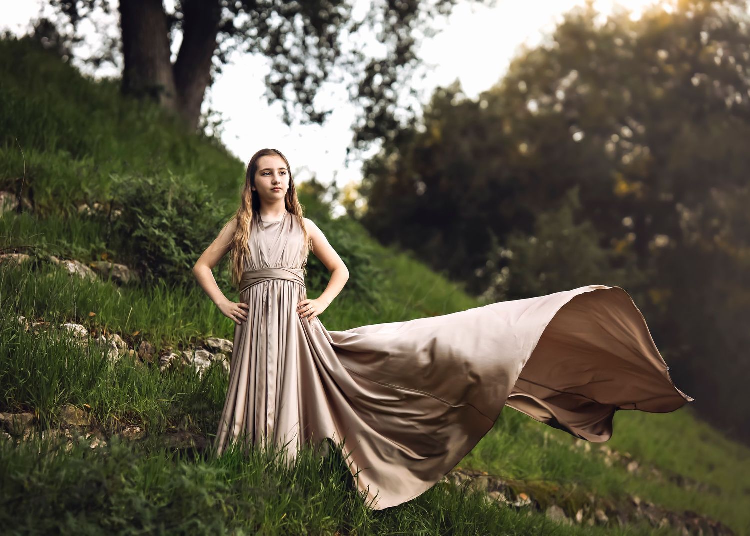 A flowing maxi dress catches the wind as a woman poses on a hillside during golden hour.