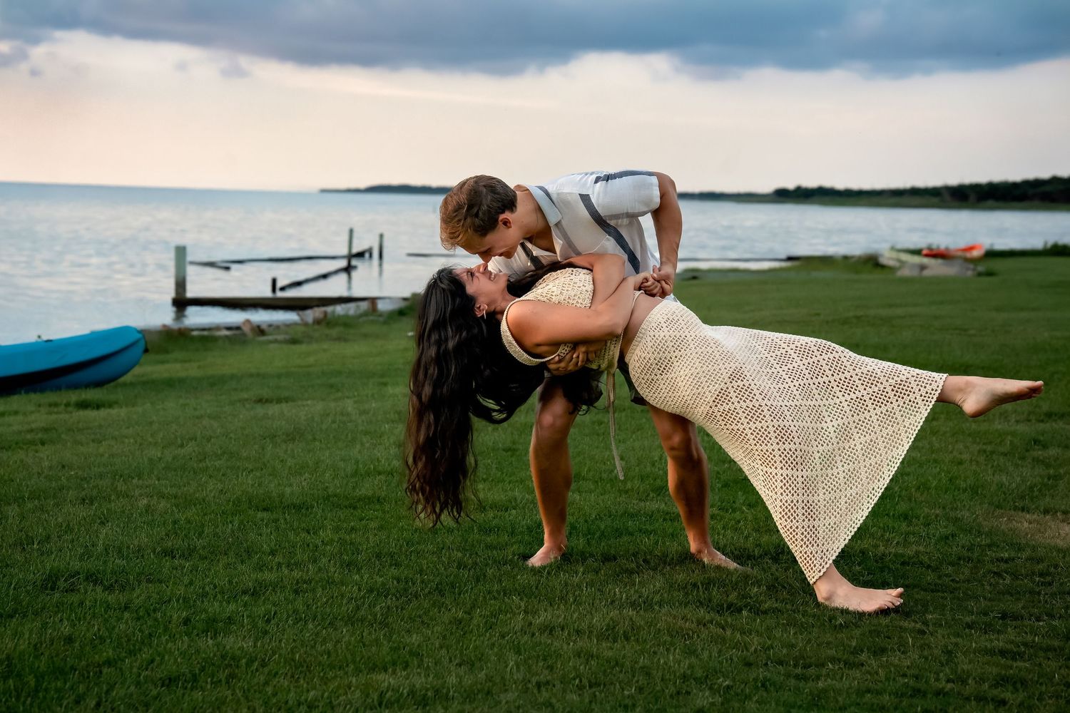 Couple playing and dancing on waterfront lawn at sunset.